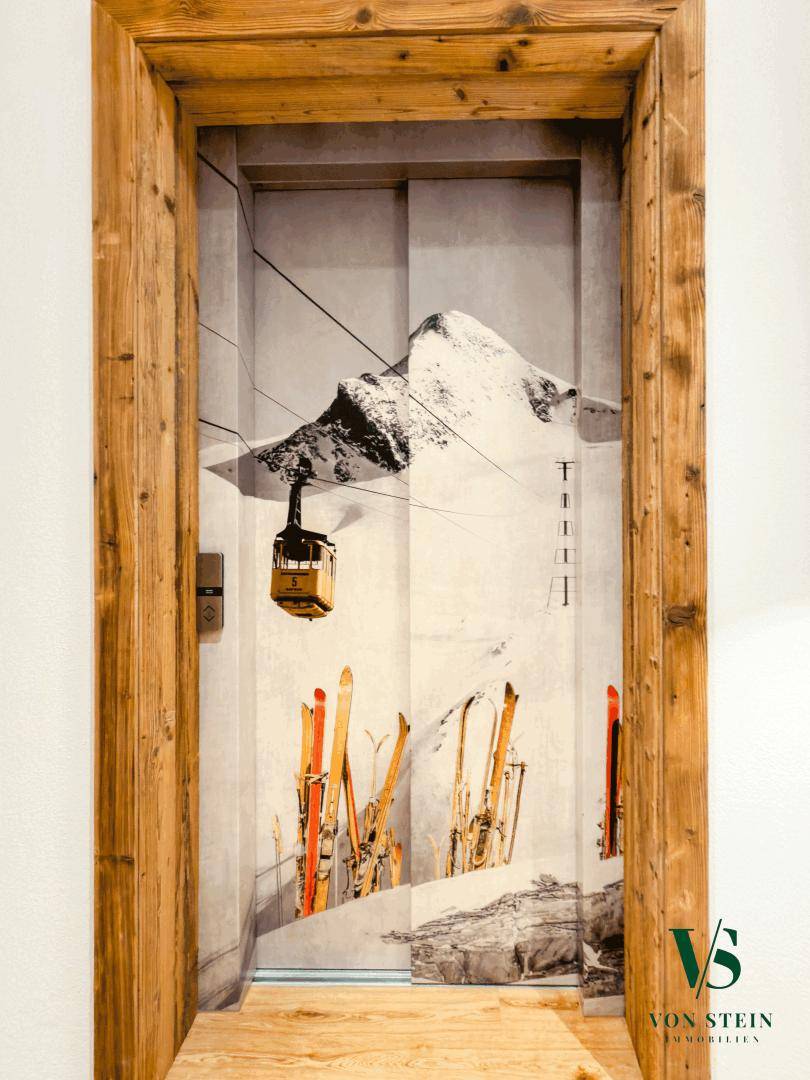 Aufzugstür mit einem dekorativen Motiv einer verschneiten Berglandschaft und Skiern.