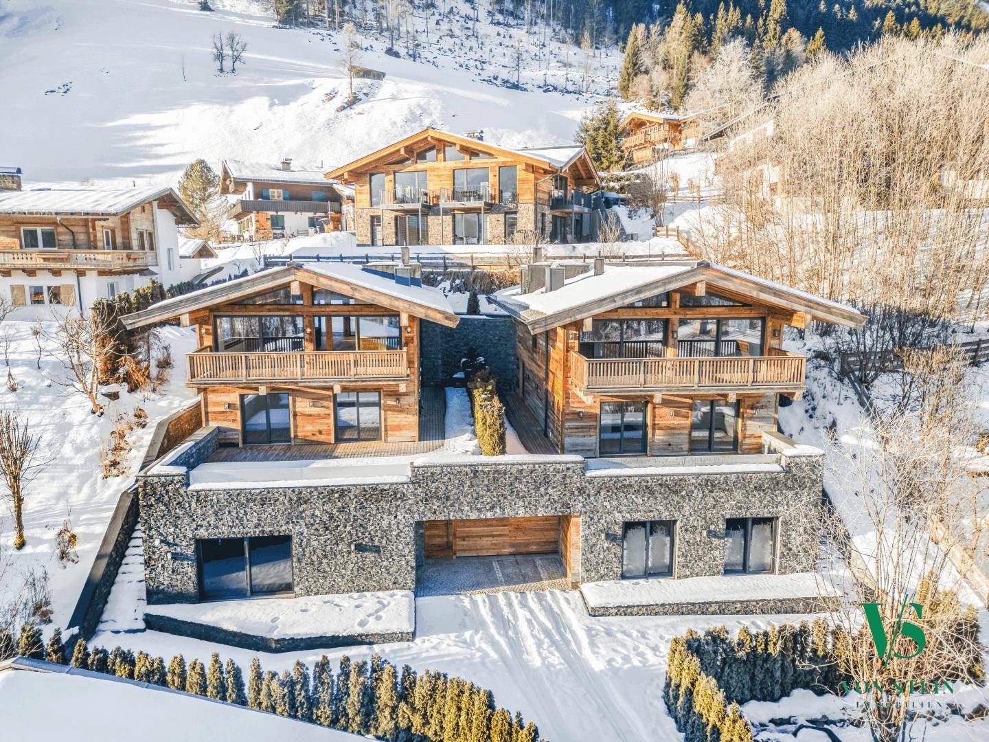 Zwei moderne Holzchalets in alpiner Winterlandschaft mit großen Glasfronten und integrierten Garagen.