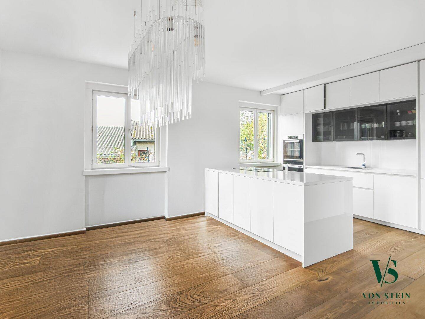Moderne, helle Küche mit weißer Kücheninsel, integrierten Geräten und elegantem Parkettboden.
