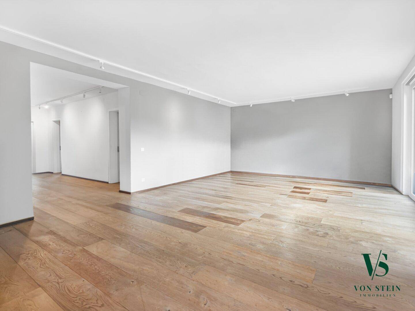 Geräumiger, leerer Wohnbereich mit hellem Parkettboden und einer modernen grauen Akzentwand.