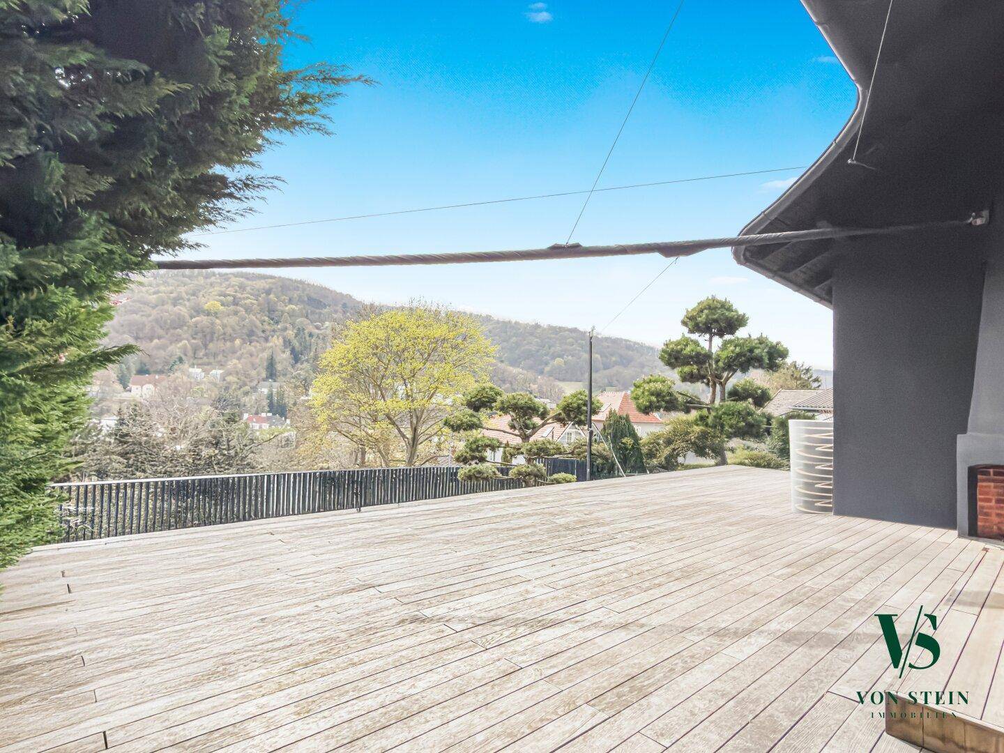 Weitläufige Holzterrasse mit Panoramablick auf die grüne Umgebung und die darunterliegenden Häuser.