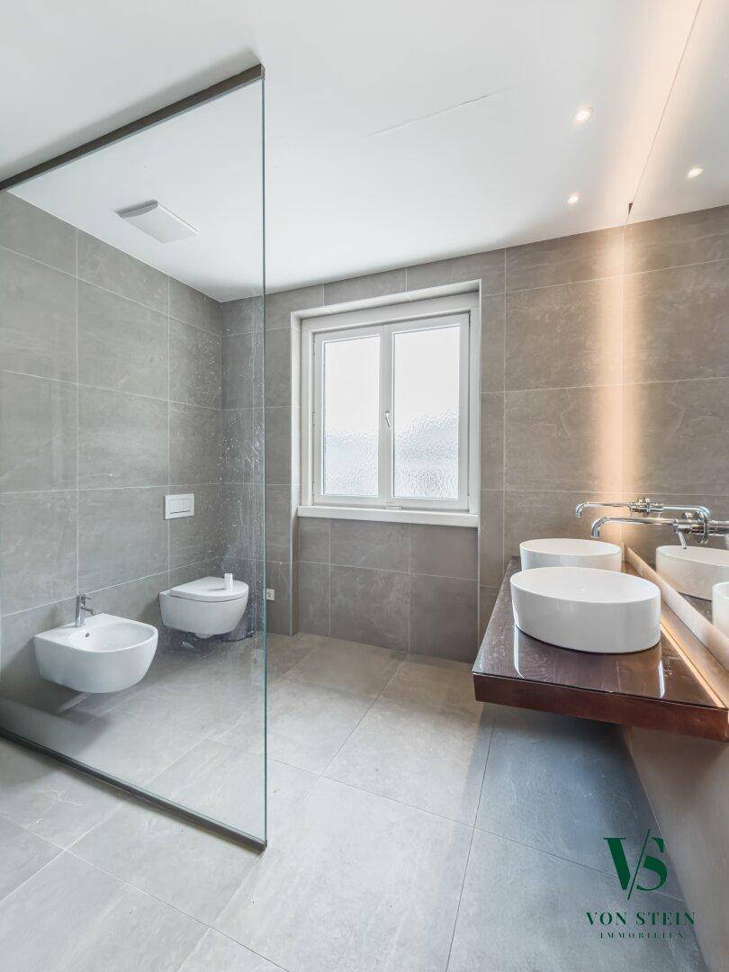 Modernes Badezimmer mit grauen Fliesen, Doppelwaschbecken, begehbarer Dusche und Bidet.