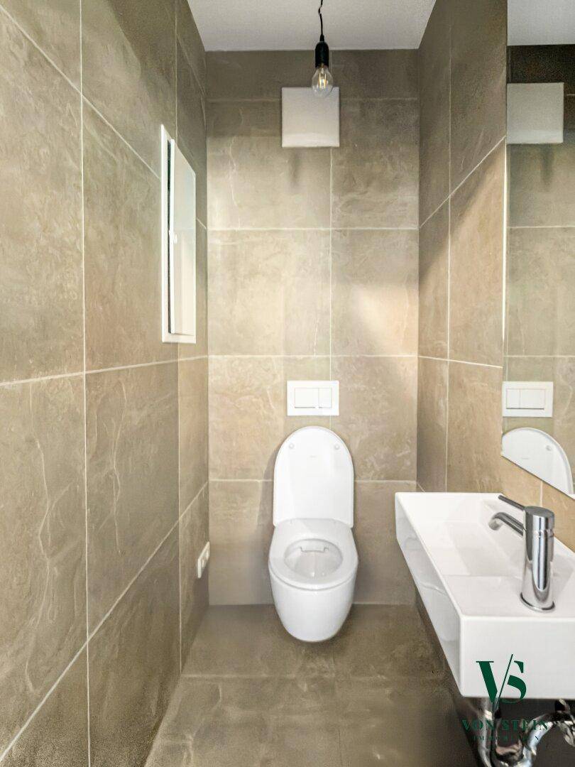 Kleines Gäste-WC mit beigefarbenen Fliesen, wandhängendem WC und modernem Waschbecken.