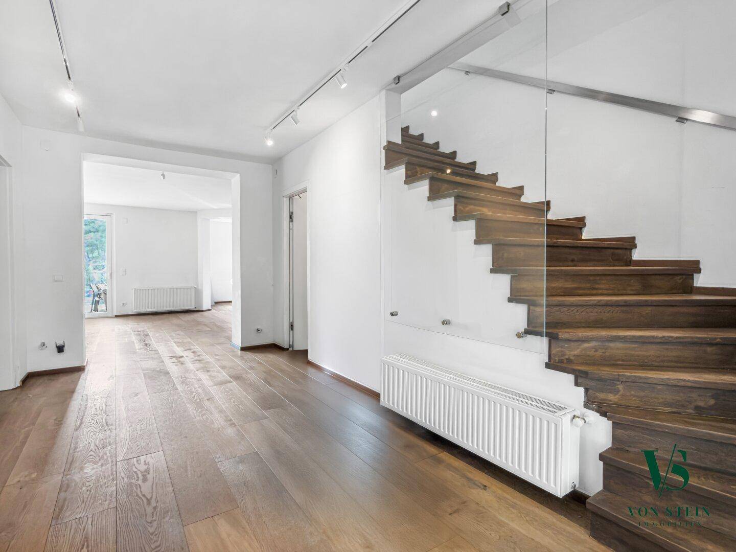 Heller Eingangsbereich mit eleganter Holztreppe, Glasgeländer und hochwertigem Parkettboden.