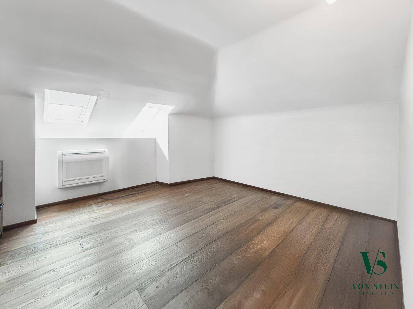 Helles Dachzimmer mit schrägen Wänden, Dachfenstern und einer Klimaanlage.