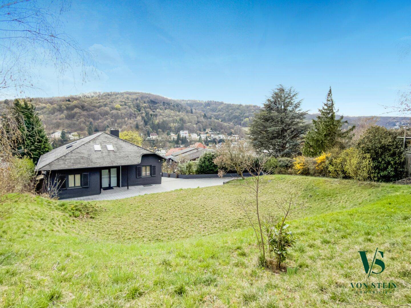 Panoramablick auf das Haus von der grünen Wiese aus mit der bewaldeten Hügellandschaft im Hintergrund.