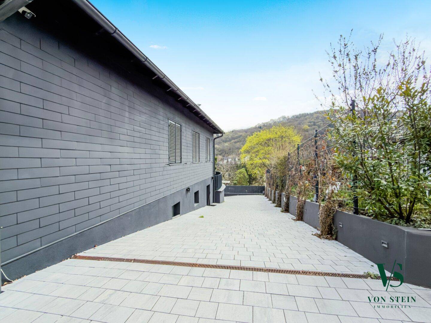 Seitenansicht des Hauses mit gepflastertem Weg und einer modernen Fassadenverkleidung.