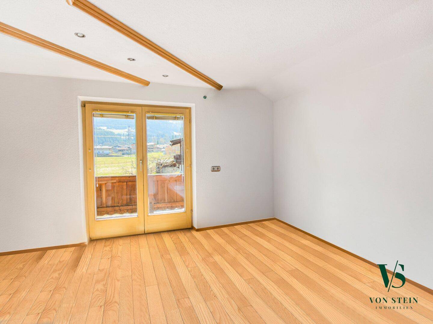 Helles Schlafzimmer mit Parkettboden, Zugang zum Balkon und Blick auf die umliegende Landschaft.