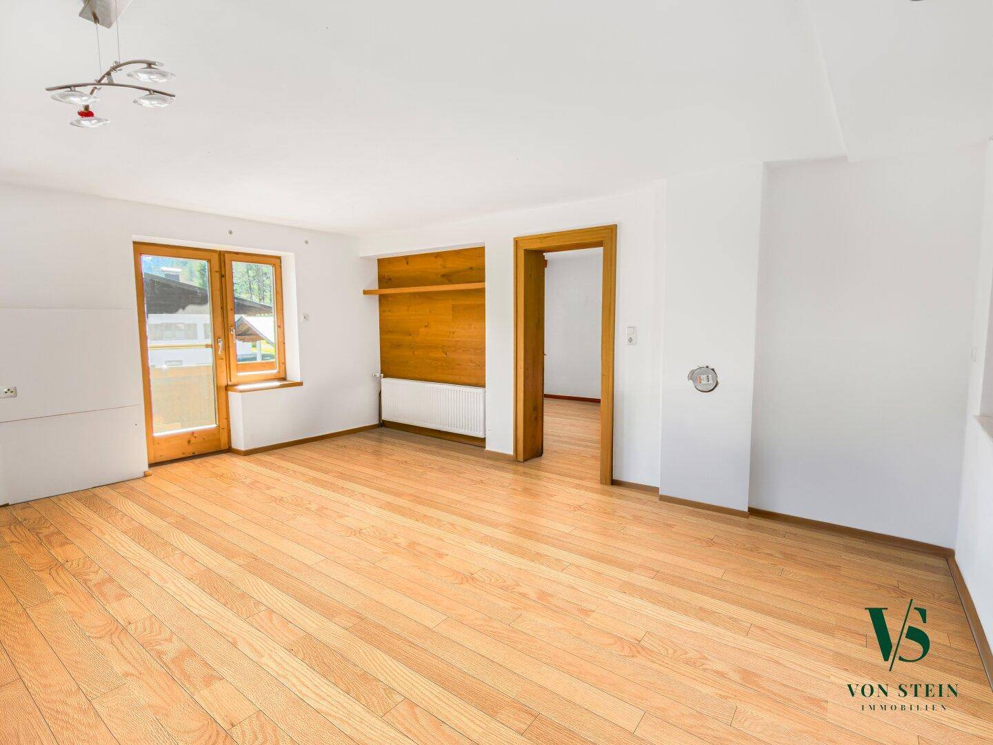 Geräumiger Wohnbereich mit Parkettboden, Holzelementen und Zugang zu einem sonnigen Balkon.