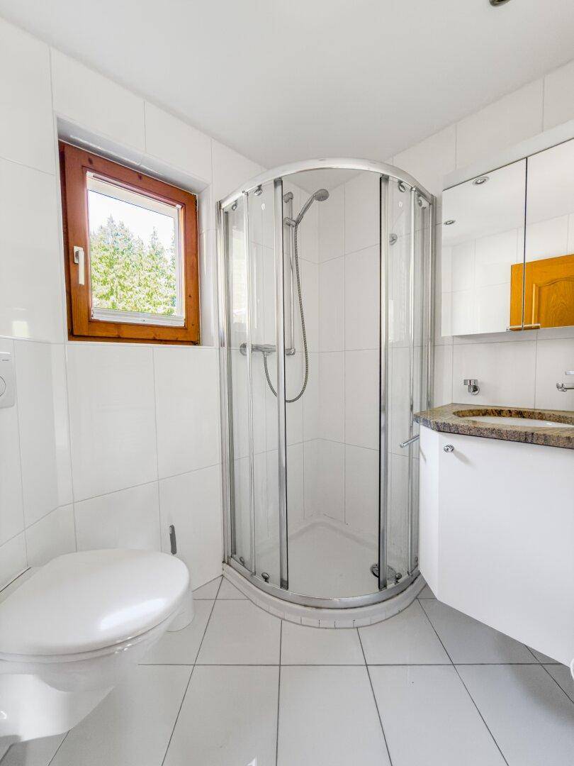 Helles Badezimmer mit Duschkabine, WC, Waschbecken und Fenster für natürliche Belüftung.