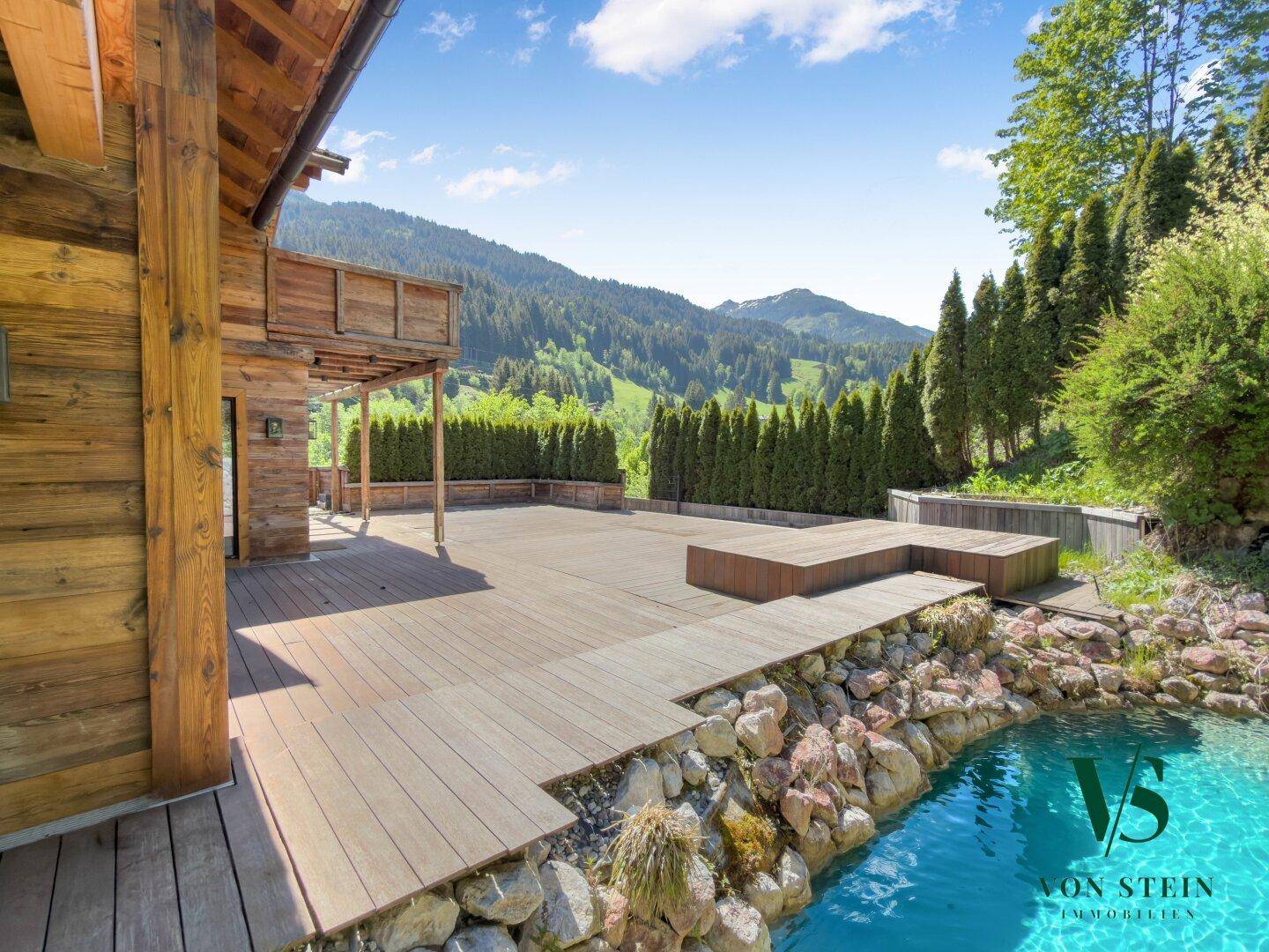 Weitläufige Holzterrasse mit Blick auf die umliegende Berglandschaft und üppiges Grün.