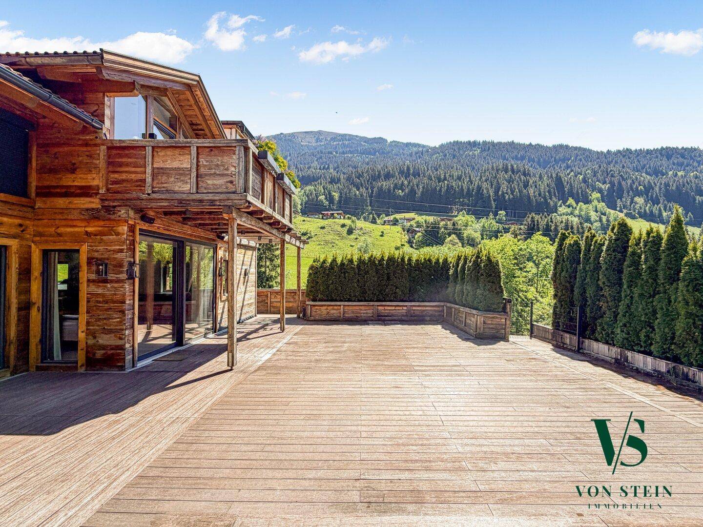 Weitläufige Holzterrasse mit Blick auf die umliegende Berglandschaft und das charmante Holzhaus.