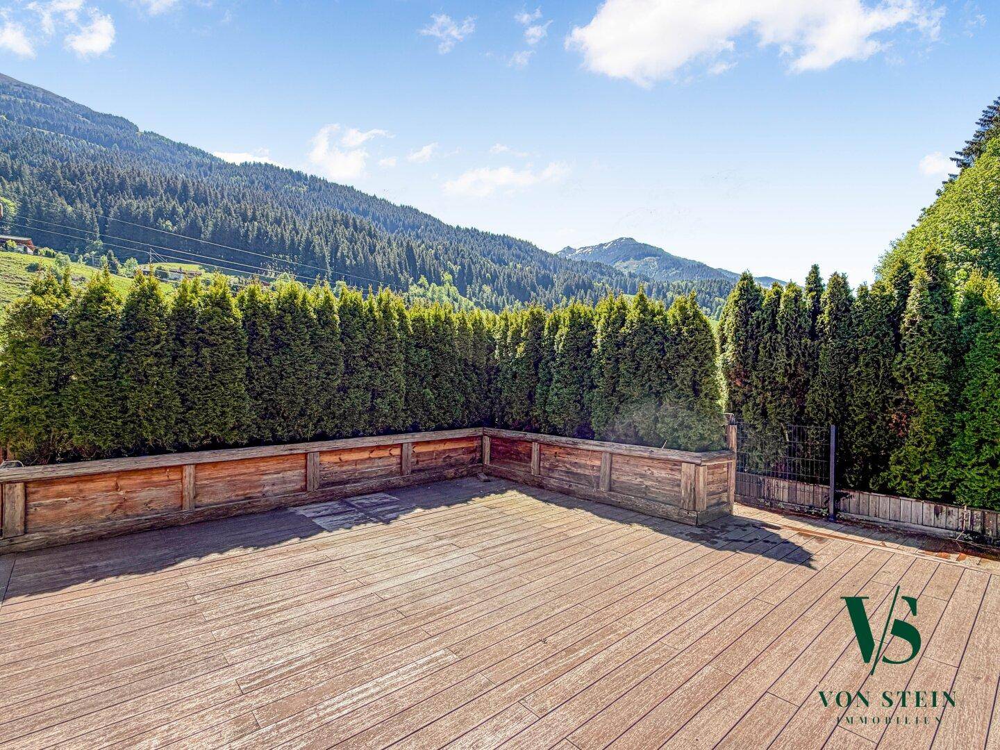 Große Holzterrasse mit hoher Hecke für Privatsphäre und weitem Blick auf die Berge.