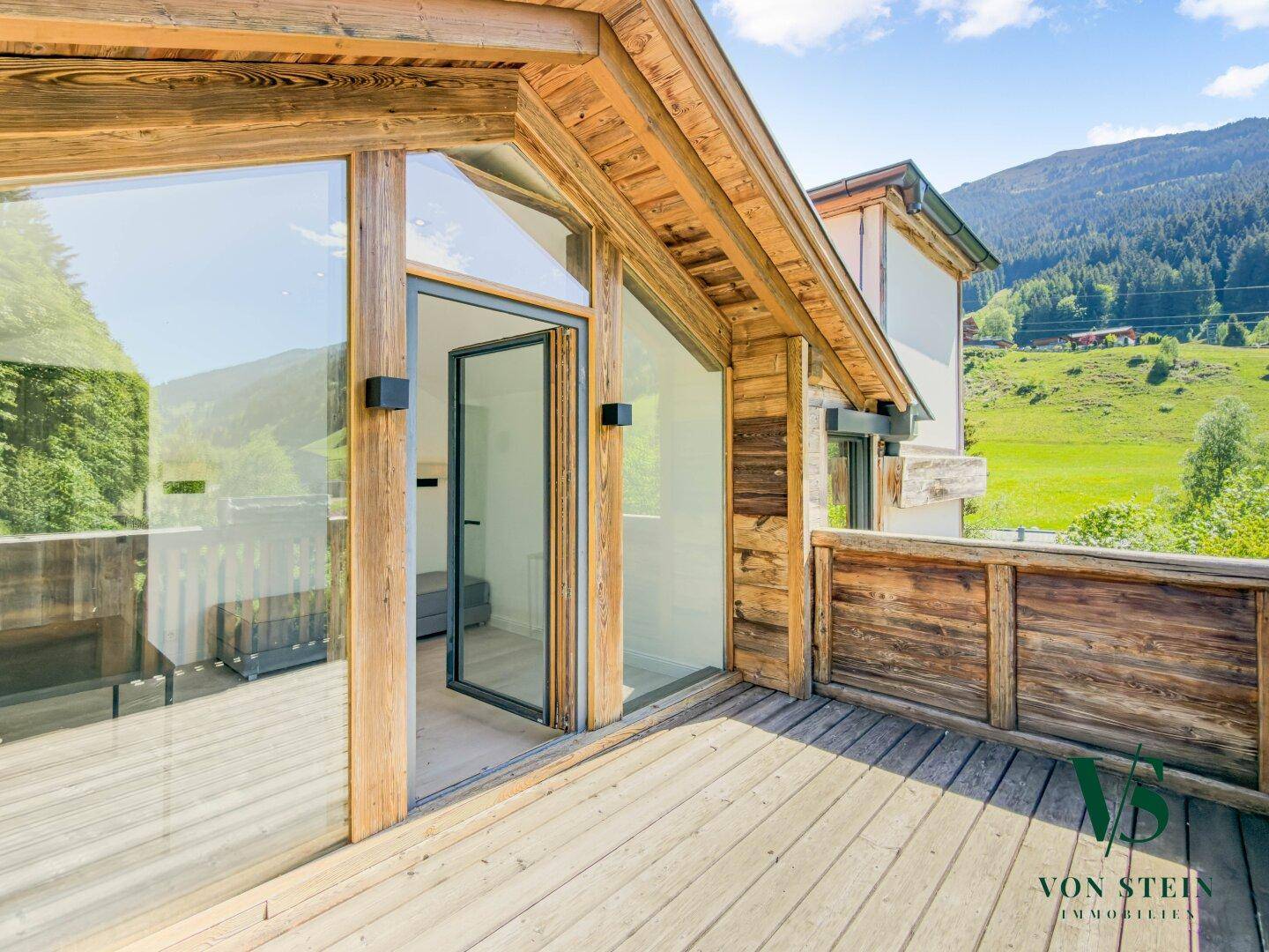 Geräumiger Holzbalkon mit großen Glasfronten und Panoramablick auf die grüne Berglandschaft.