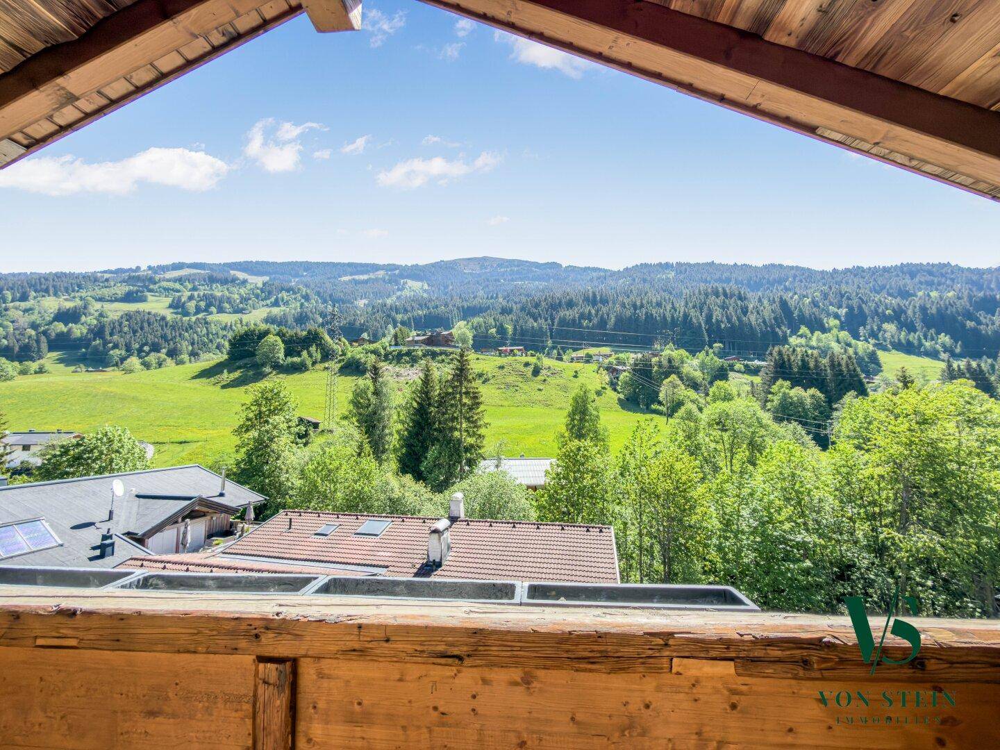 Balkon mit Panoramablick über die hügelige Landschaft und bewaldete Berge unter blauem Himmel.