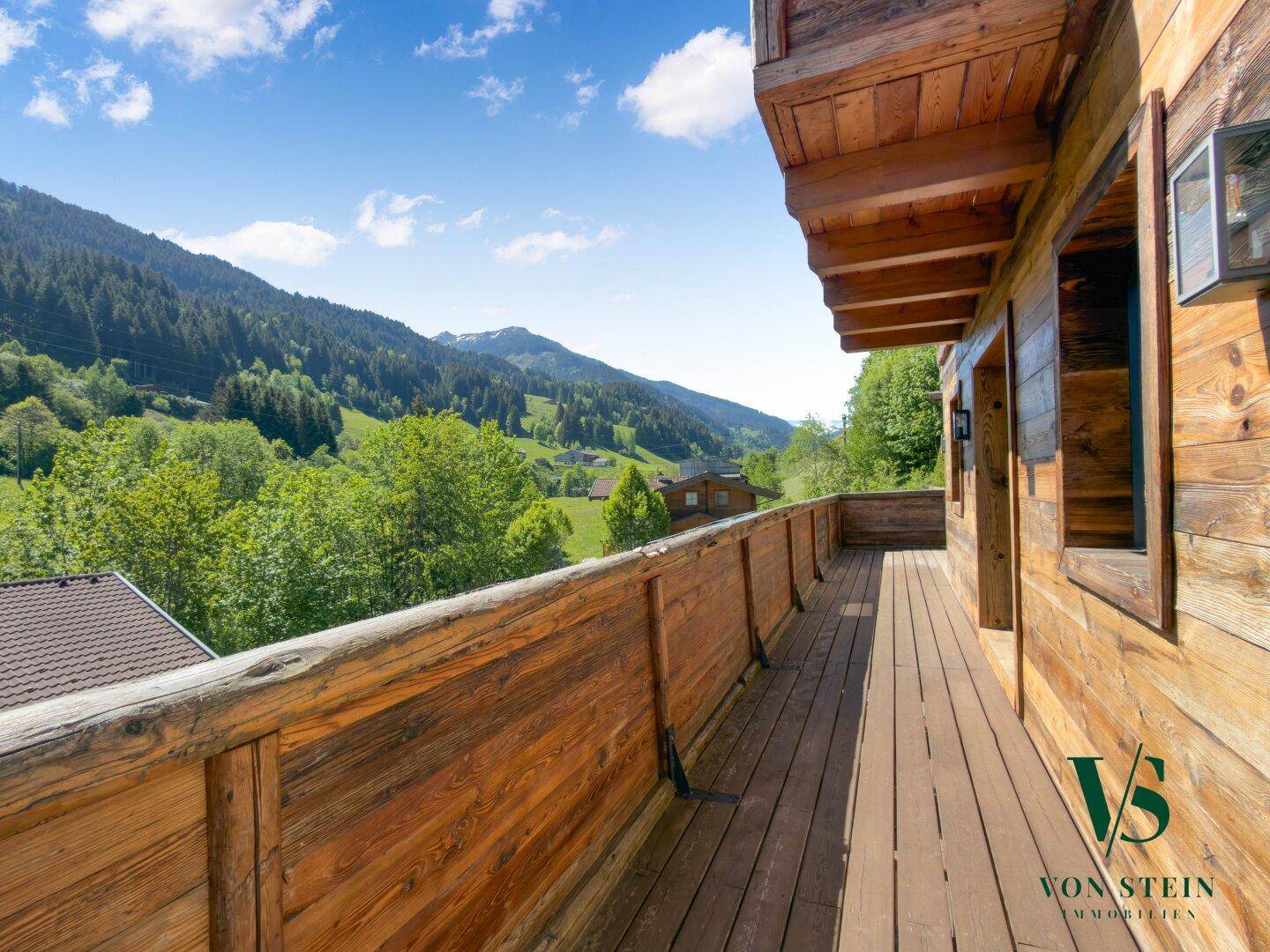 Langer Holzbalkon mit rustikalem Geländer und weitem Blick auf die grüne Berglandschaft.