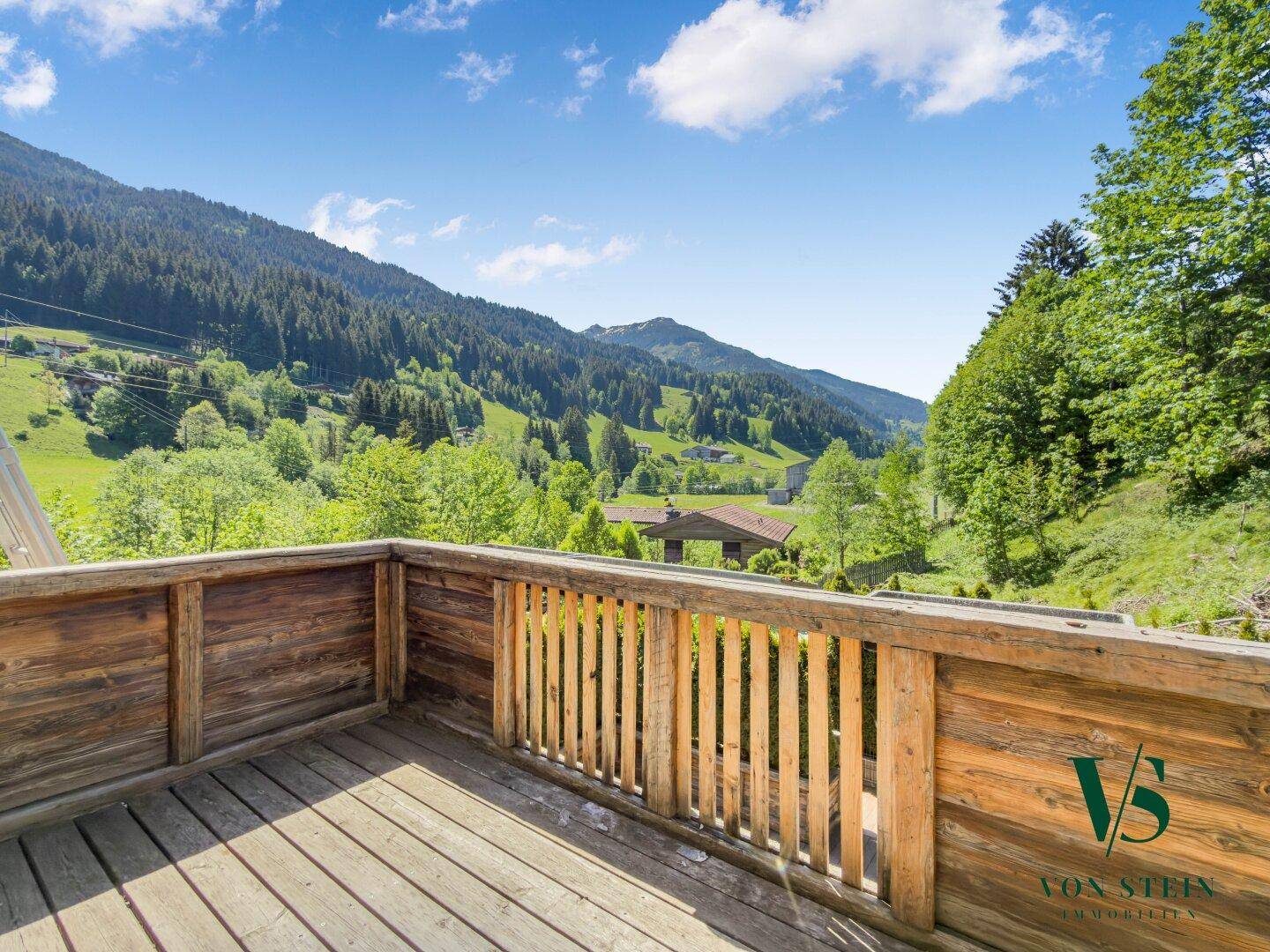 Großer Holzbalkon mit rustikalem Geländer und weitem Blick auf die umliegende Bergwelt.