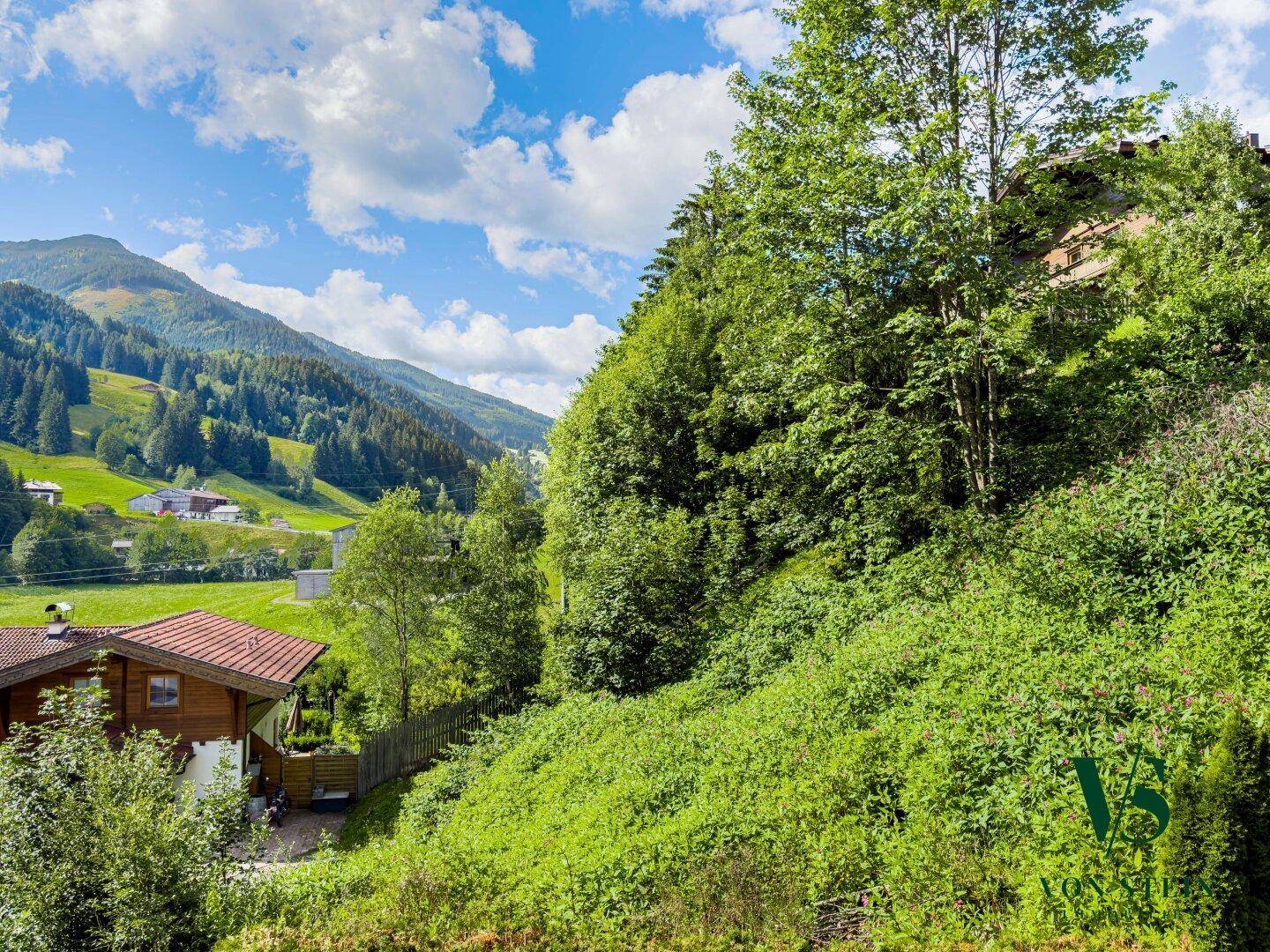 Grüne Hügellandschaft mit üppiger Vegetation und einem Teil des Hauses im Vordergrund.