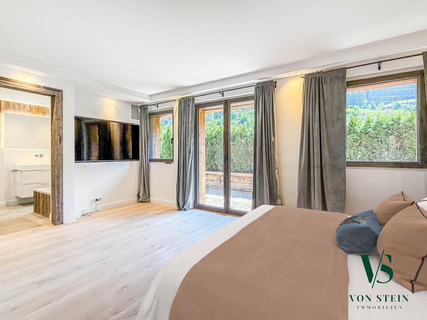 Geräumiges Schlafzimmer mit großem Bett, Fernseher und Blick ins Grüne durch große Fenster.