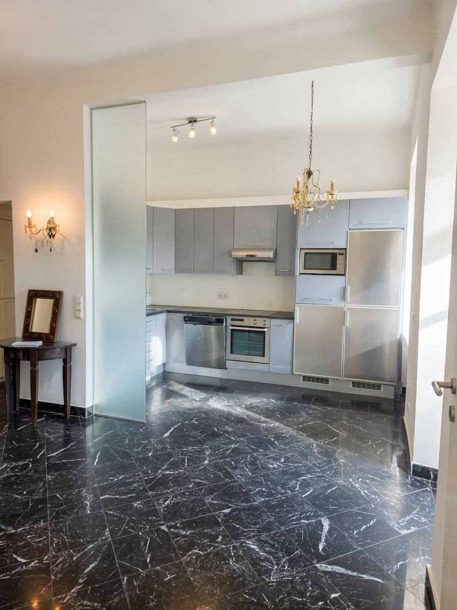 Moderne Küche mit grauen Hochglanzfronten, Einbaugeräten und dunklem Marmorboden.