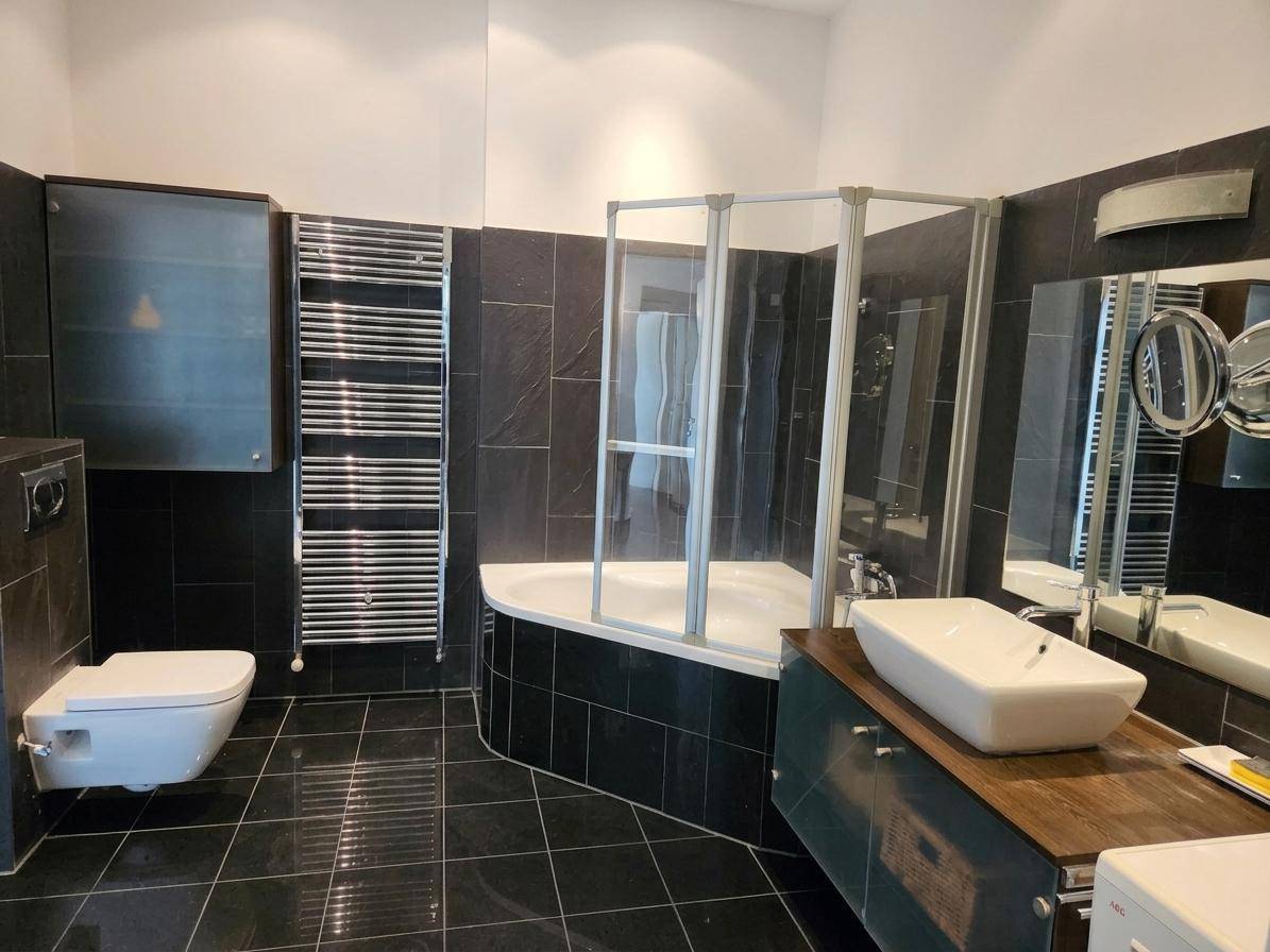 Modernes Badezimmer mit dunklen Fliesen, Badewanne, Dusche und beheiztem Handtuchhalter.