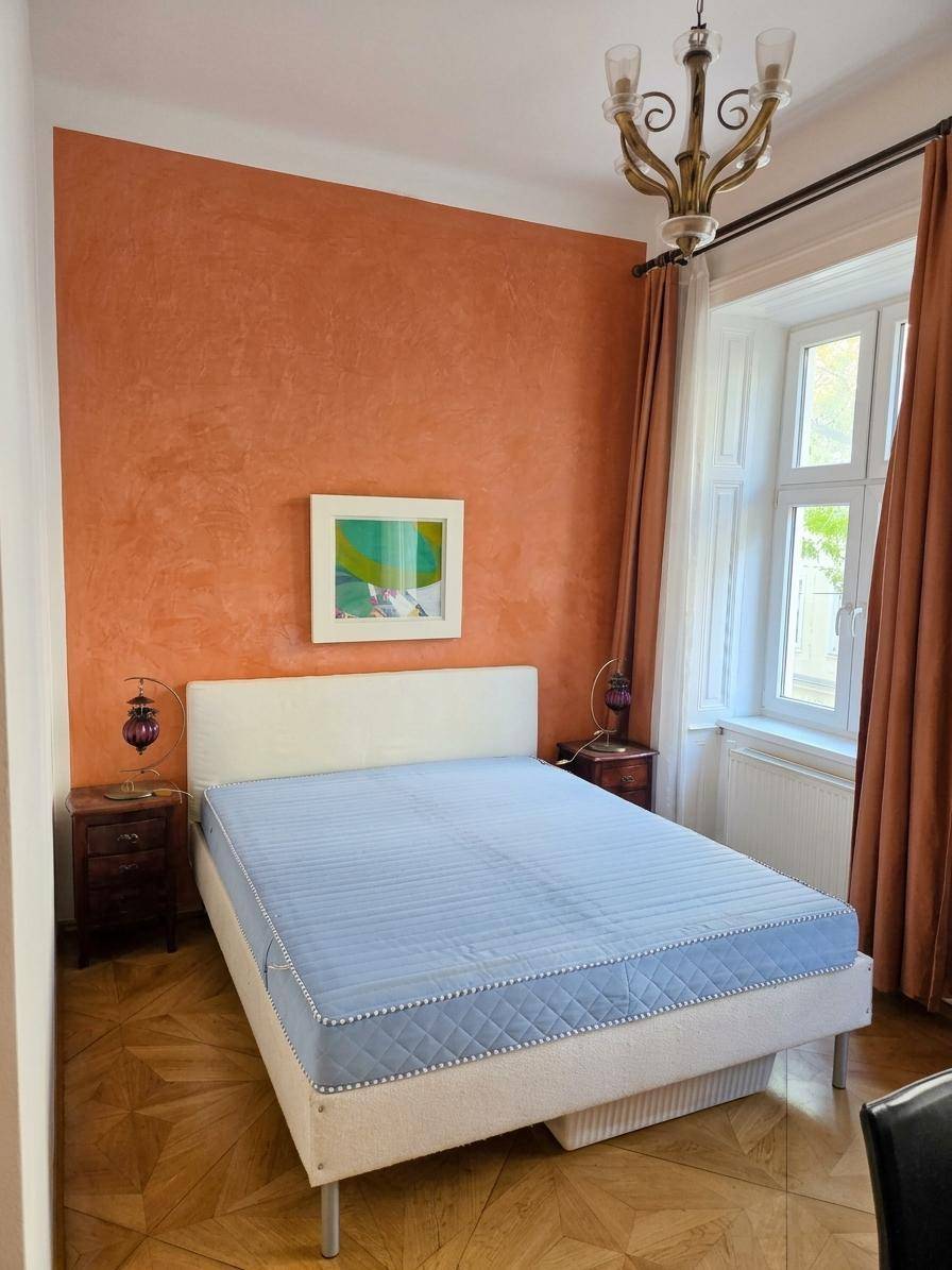 Gemütliches Schlafzimmer mit Parkettboden, orangefarbener Akzentwand und Doppelbett.