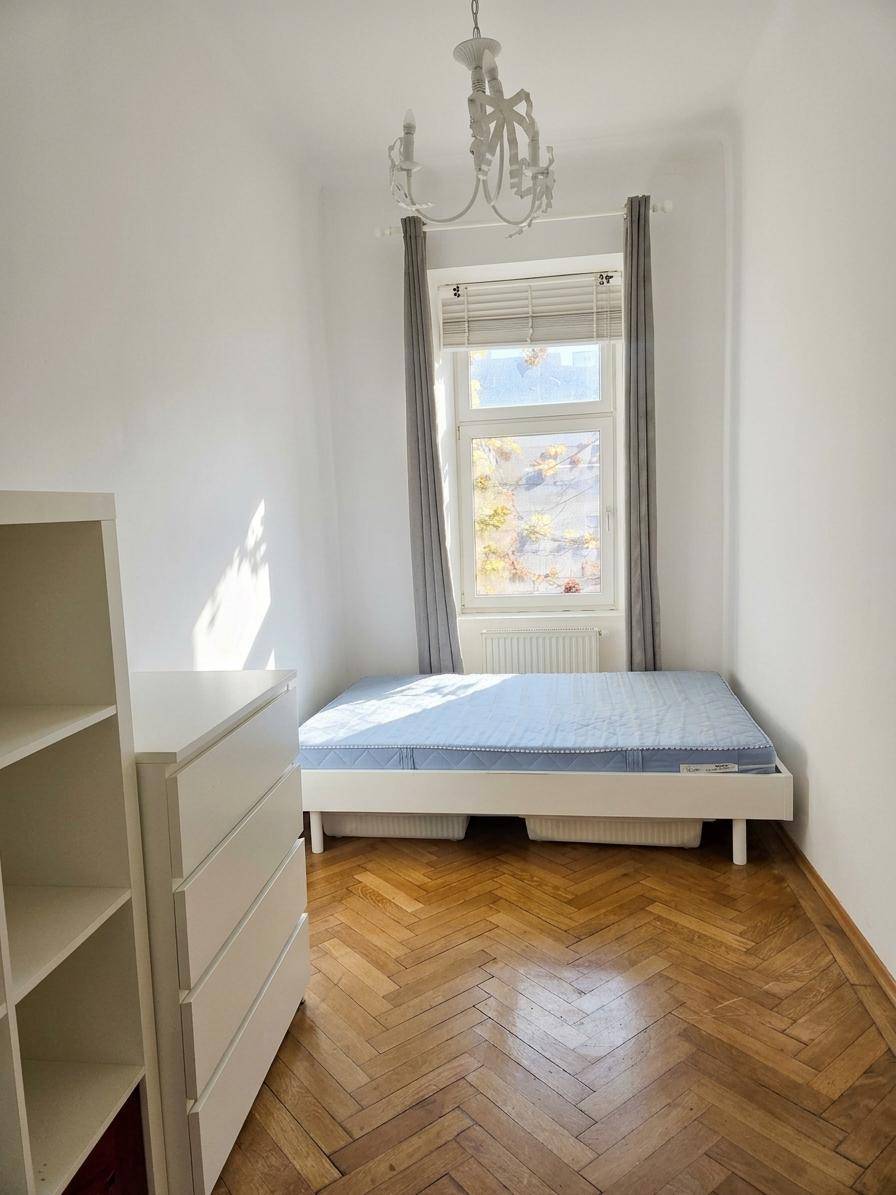 Helles Schlafzimmer mit Fischgrätparkett, Einzelbett und großem Fenster.