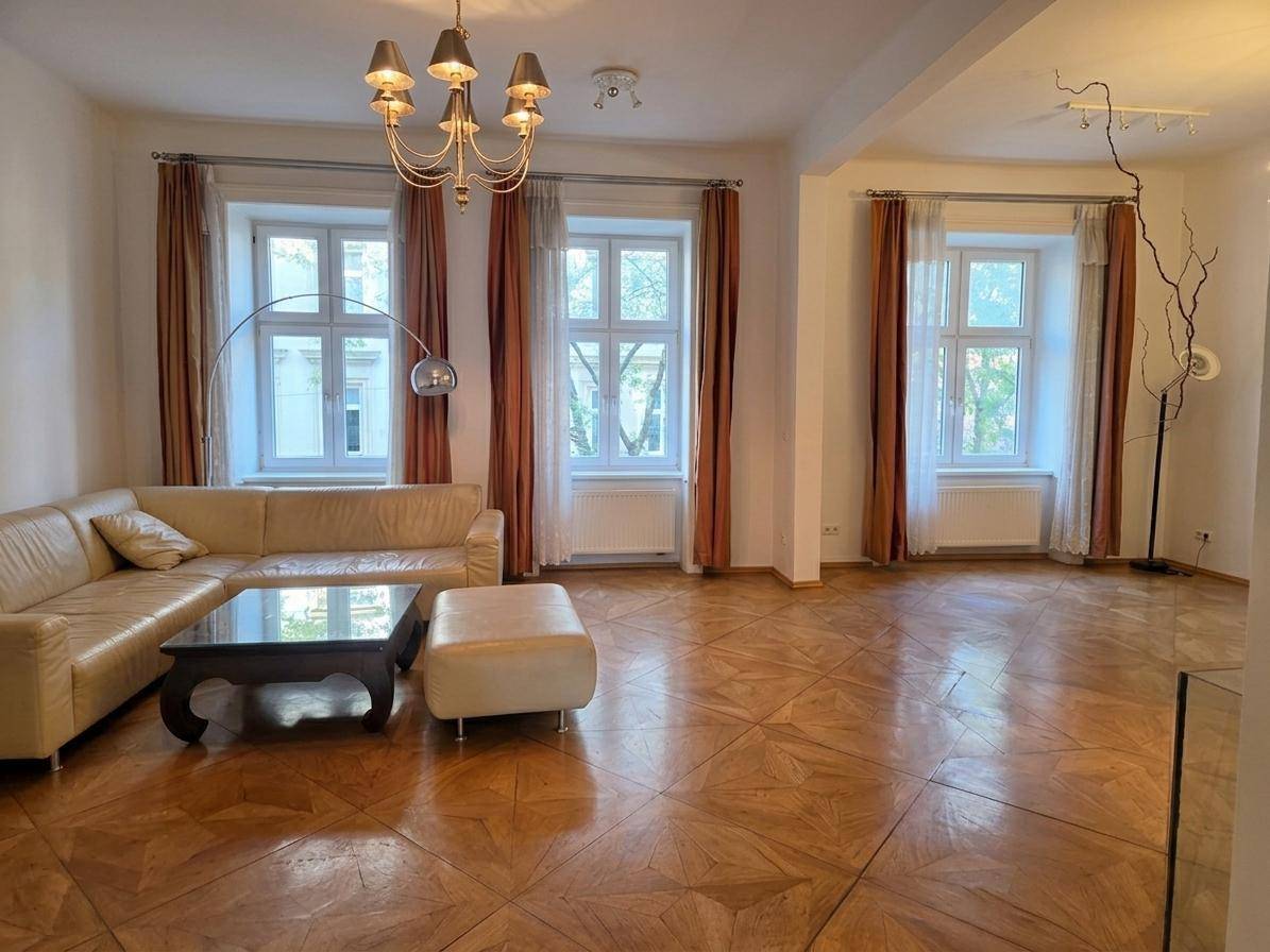 Lichtdurchflutetes Wohnzimmer mit beigem Sofa, Parkettboden und hohen Fenstern.