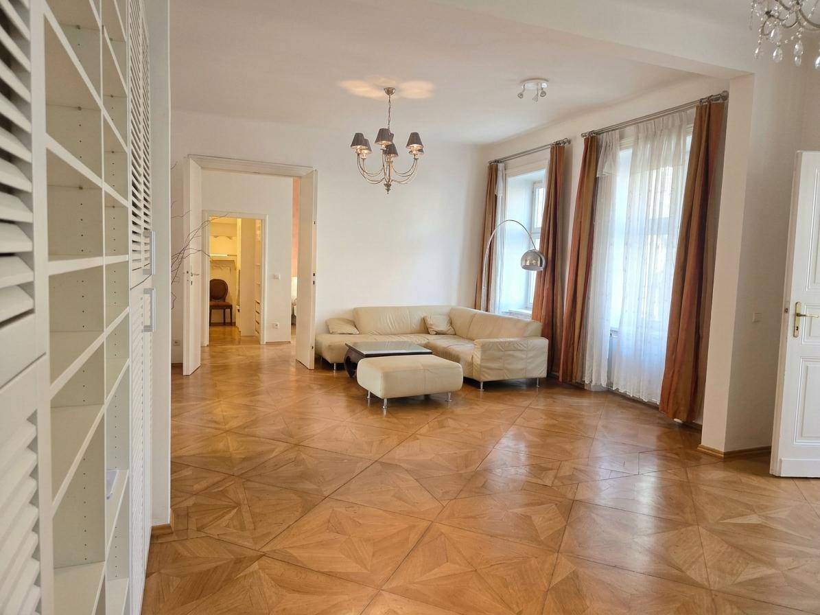 Helles Wohnzimmer mit beigem Ecksofa, Parkettboden und hohen Fenstern.