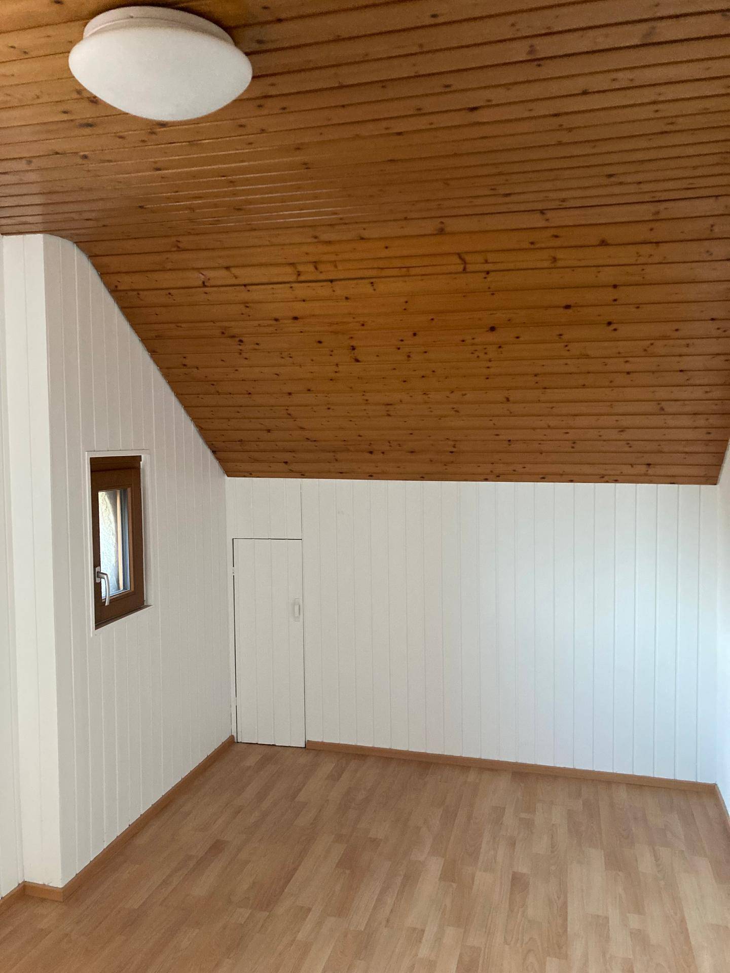 Gemütliches Zimmer mit Laminatboden, holzvertäfelten Wänden und einer charmanten Holzdecke unter dem Dach.