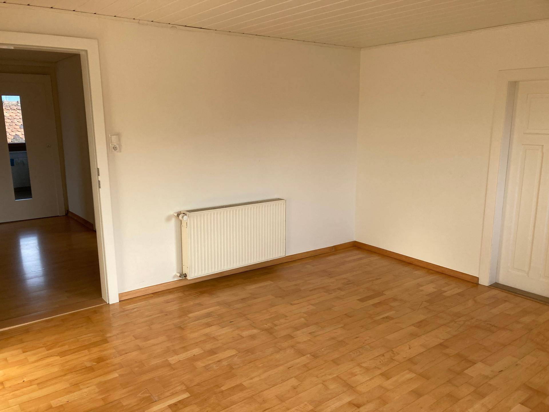 Heller Wohnraum mit klassischem Parkettboden und weiß gestrichenen Wänden, bereit zur individuellen Gestaltung.