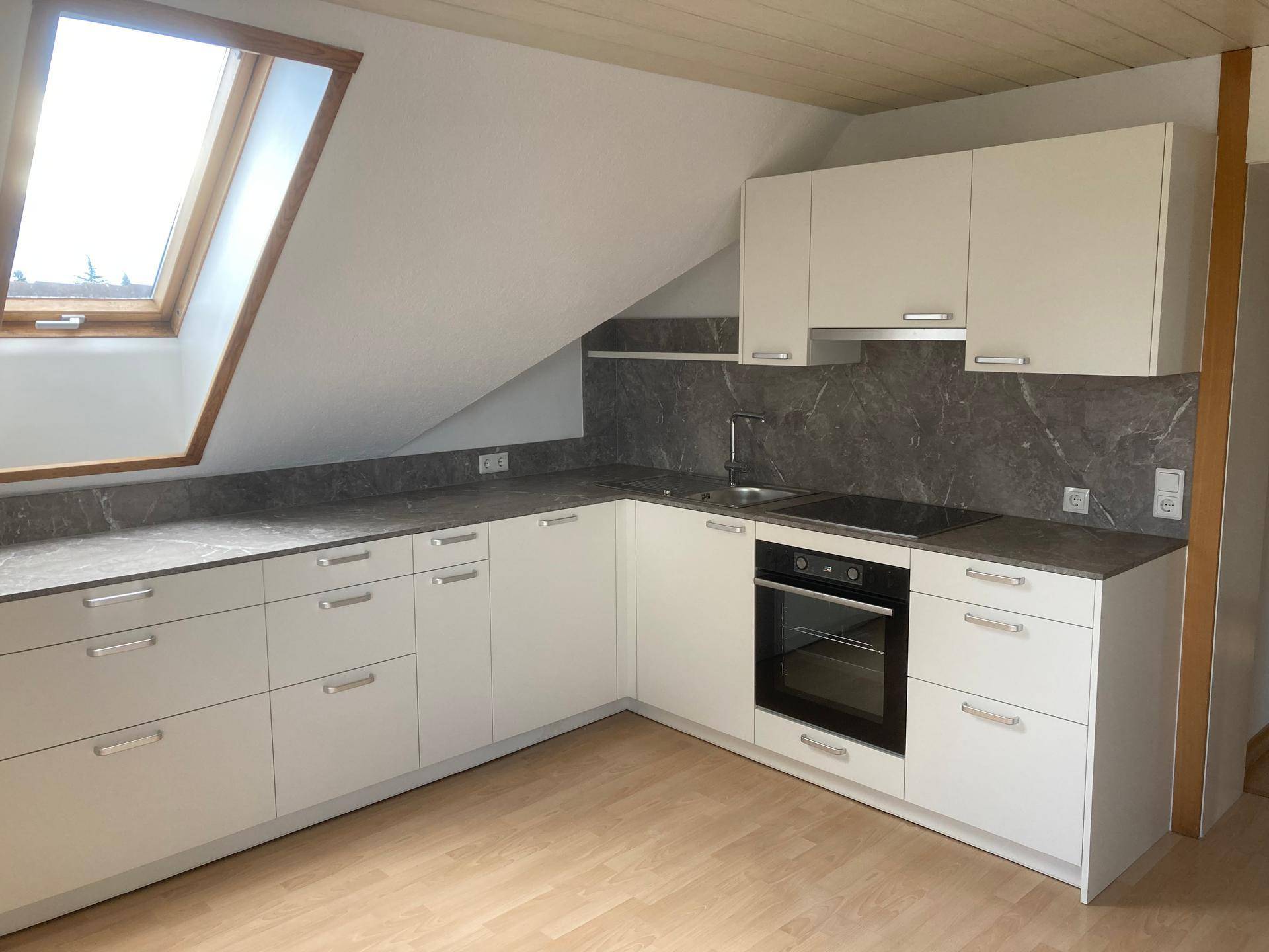 Helle Küche mit Dachfenster, weißen Schränken und Holzdecke, ideal für eine Dachgeschosswohnung.