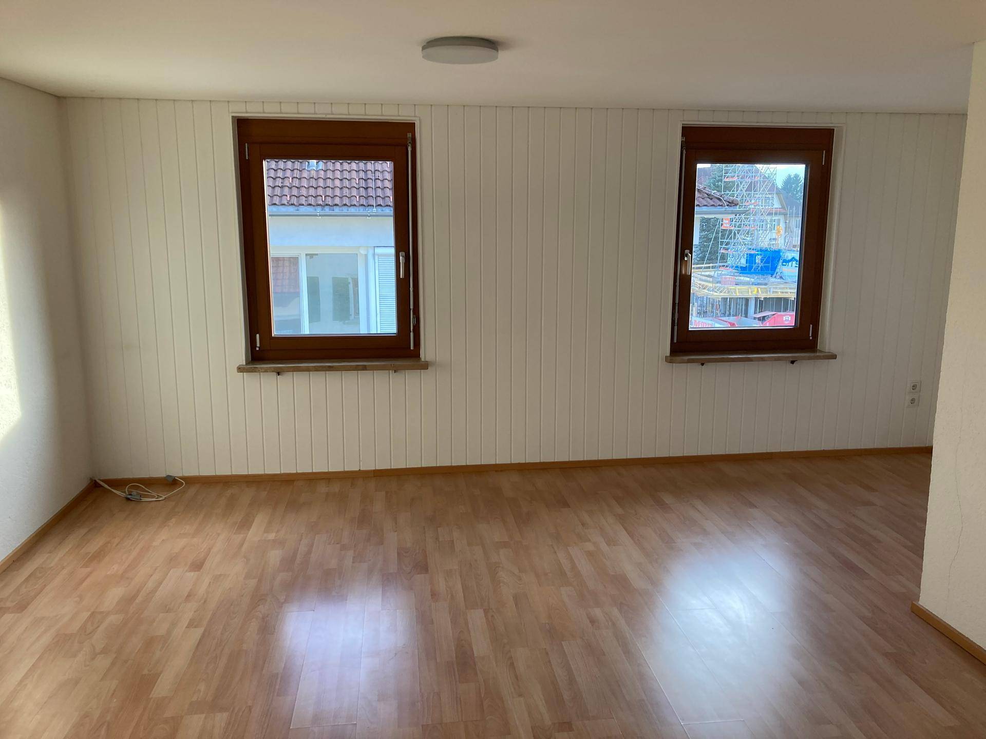 Freundlicher Raum mit Laminatboden, holzvertäfelten Wänden und zwei Fenstern für viel Tageslicht.