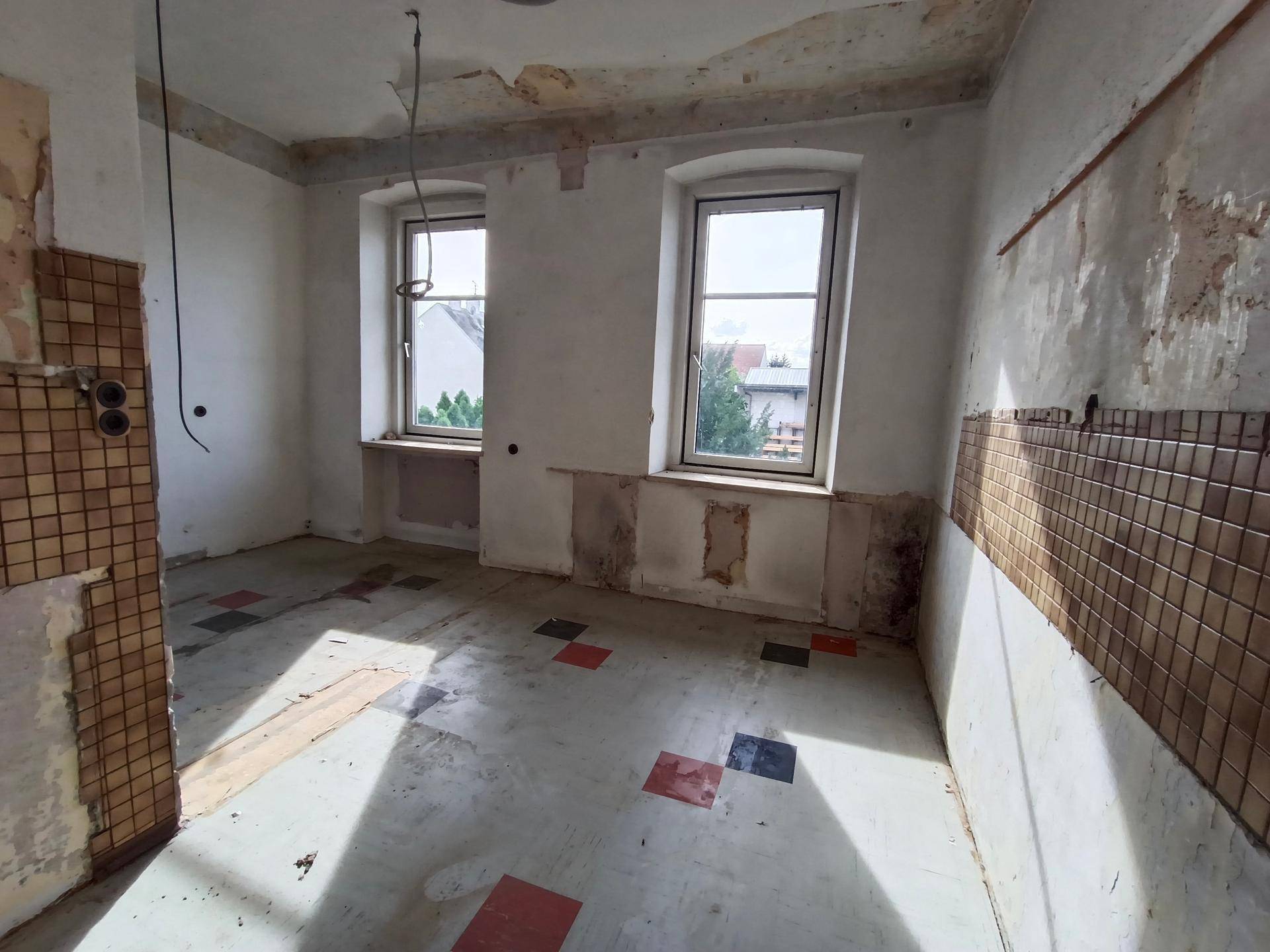Renovierungsbedürftige Küche mit alten Wandfliesen und zwei Fenstern, bereit zur Neugestaltung.