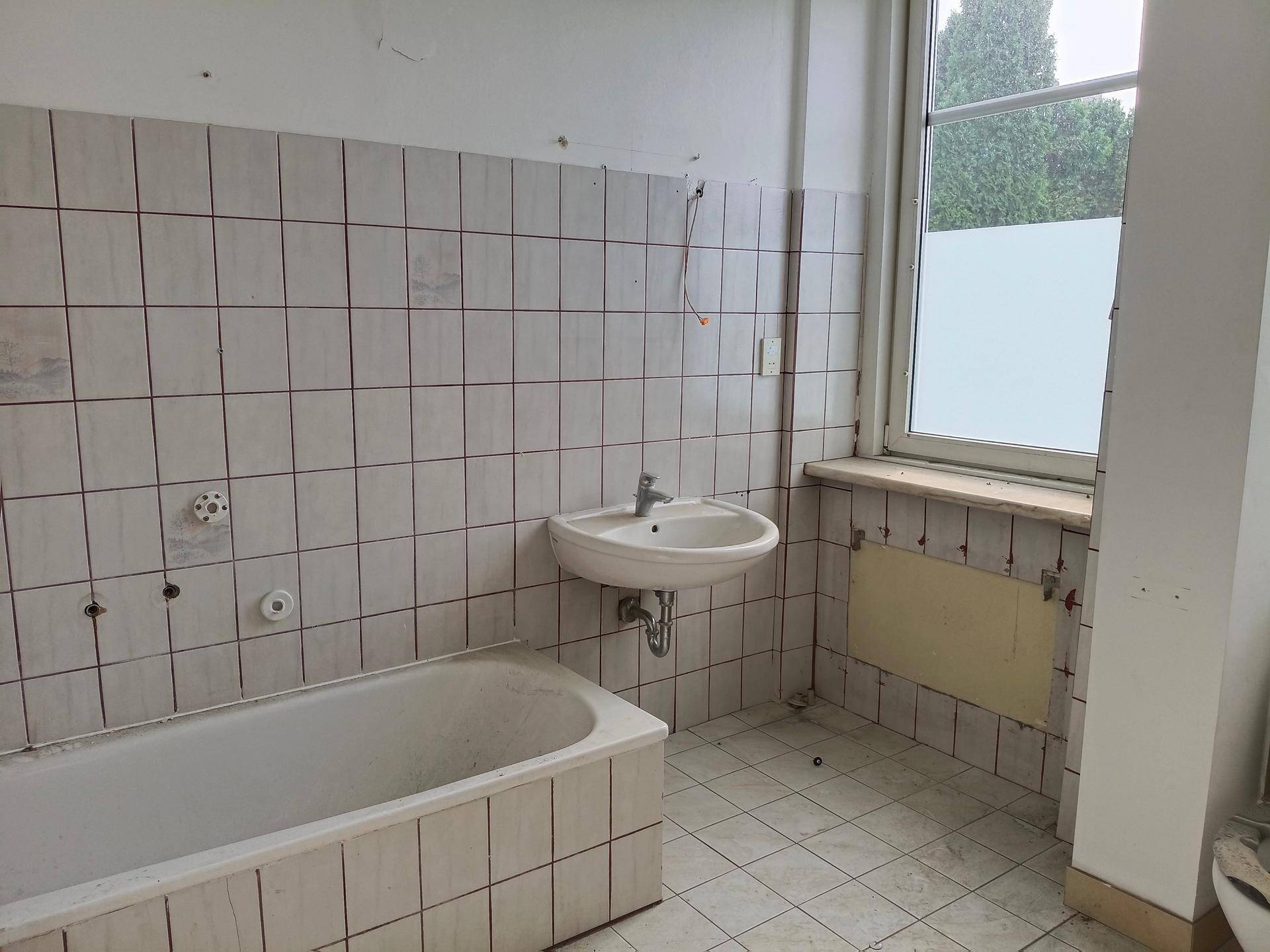 Badezimmer mit Badewanne und Waschbecken, das umfassend renoviert werden muss.