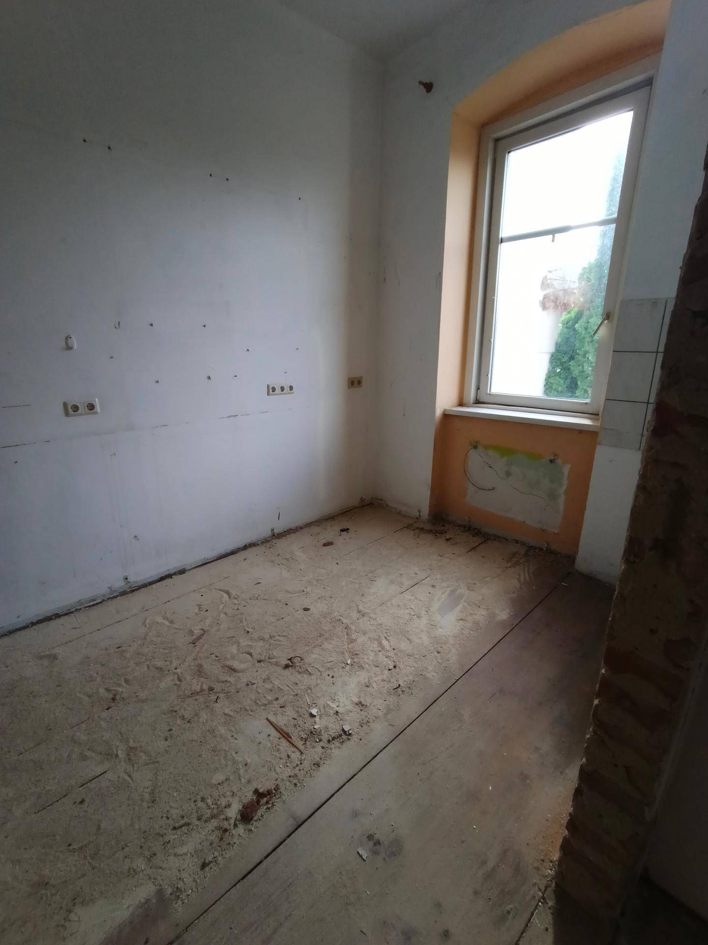 Kleiner Raum mit einem Fenster und sichtbaren Spuren von Abbrucharbeiten an den Wänden.