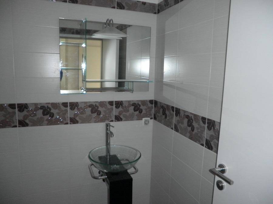 Modernes Badezimmer mit gemusterten Fliesen, Glaswaschbecken und Spiegelschrank.
