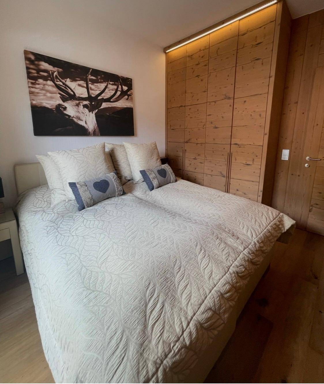 Schlafzimmer mit Holzeinbauschränken, gemütlichem Bett und Hirschgeweih-Wandbild.