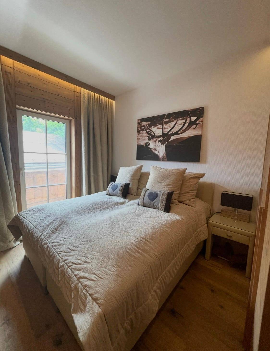 Schlafzimmer mit Holzwänden, bequemen Betten und Blick ins Grüne durch das Fenster.
