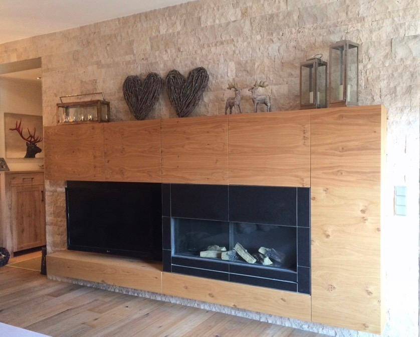 Gemütlicher Wohnbereich mit Holzeinbauten, modernem Kamin und rustikaler Steinwand.