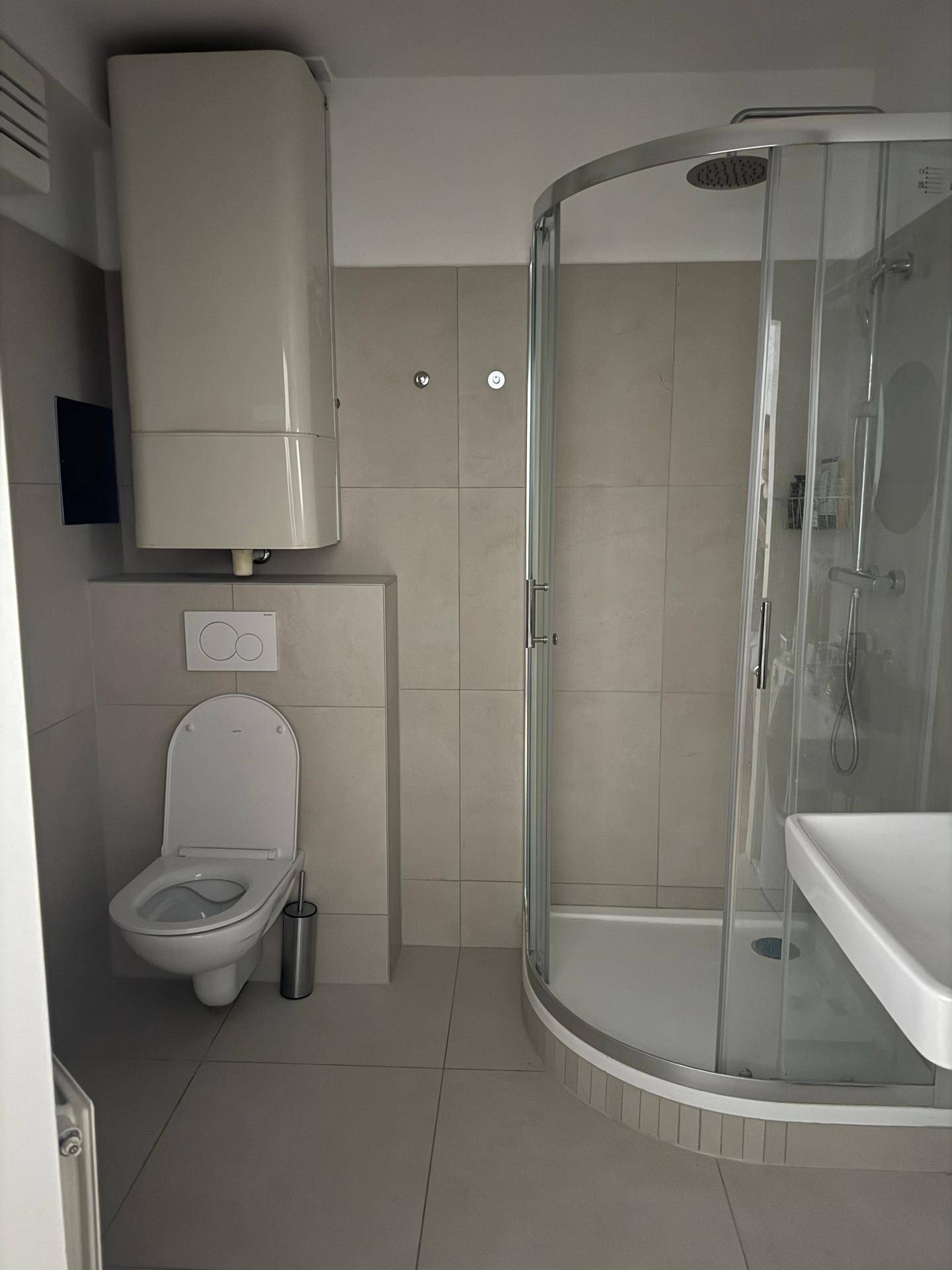 Funktionales Badezimmer mit Duschkabine, Toilette und Waschbecken, ausgestattet mit hellen Fliesen.