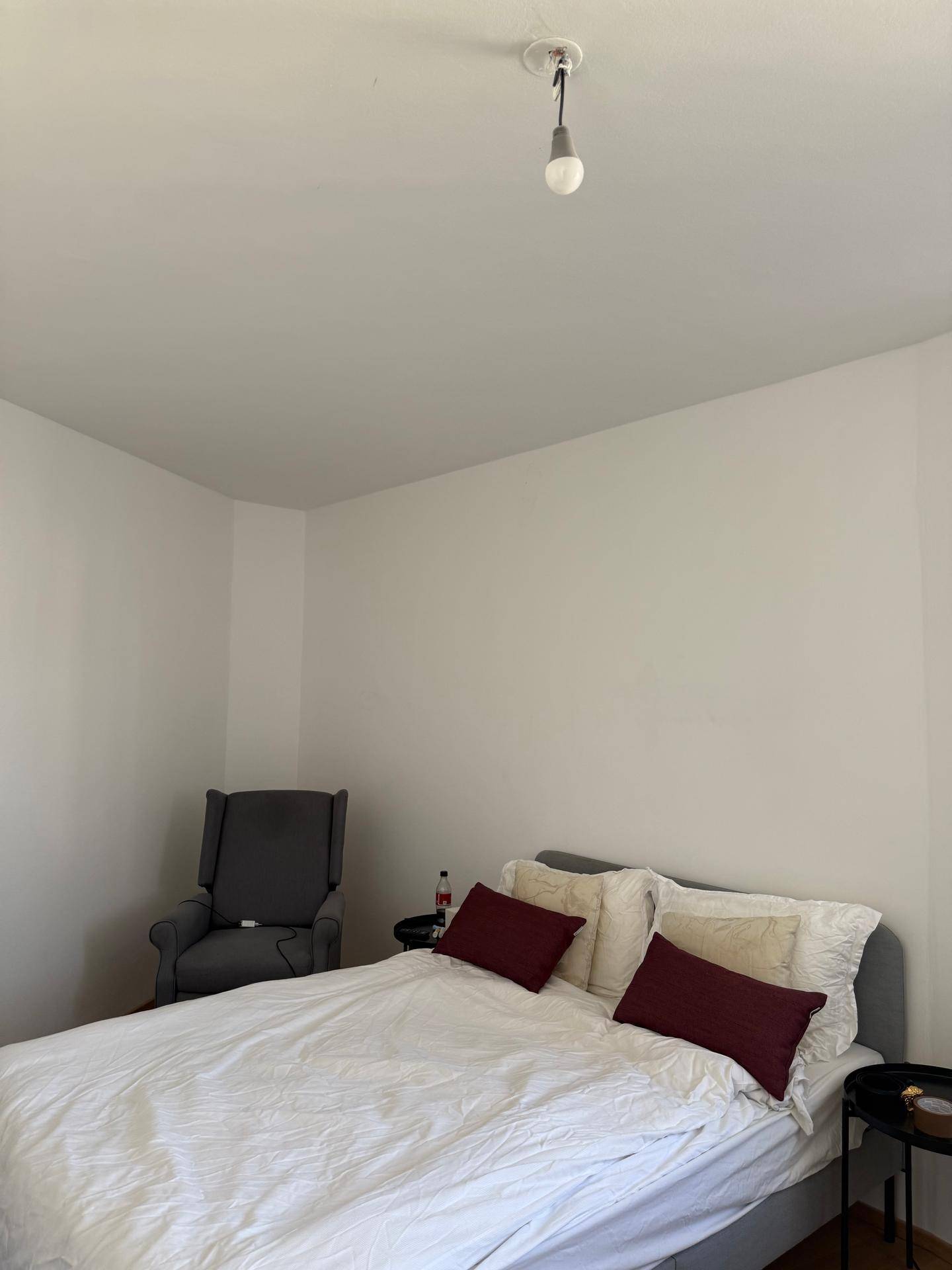 Schlafzimmer mit Doppelbett, einem Sessel und Holzboden, hell und schlicht eingerichtet.