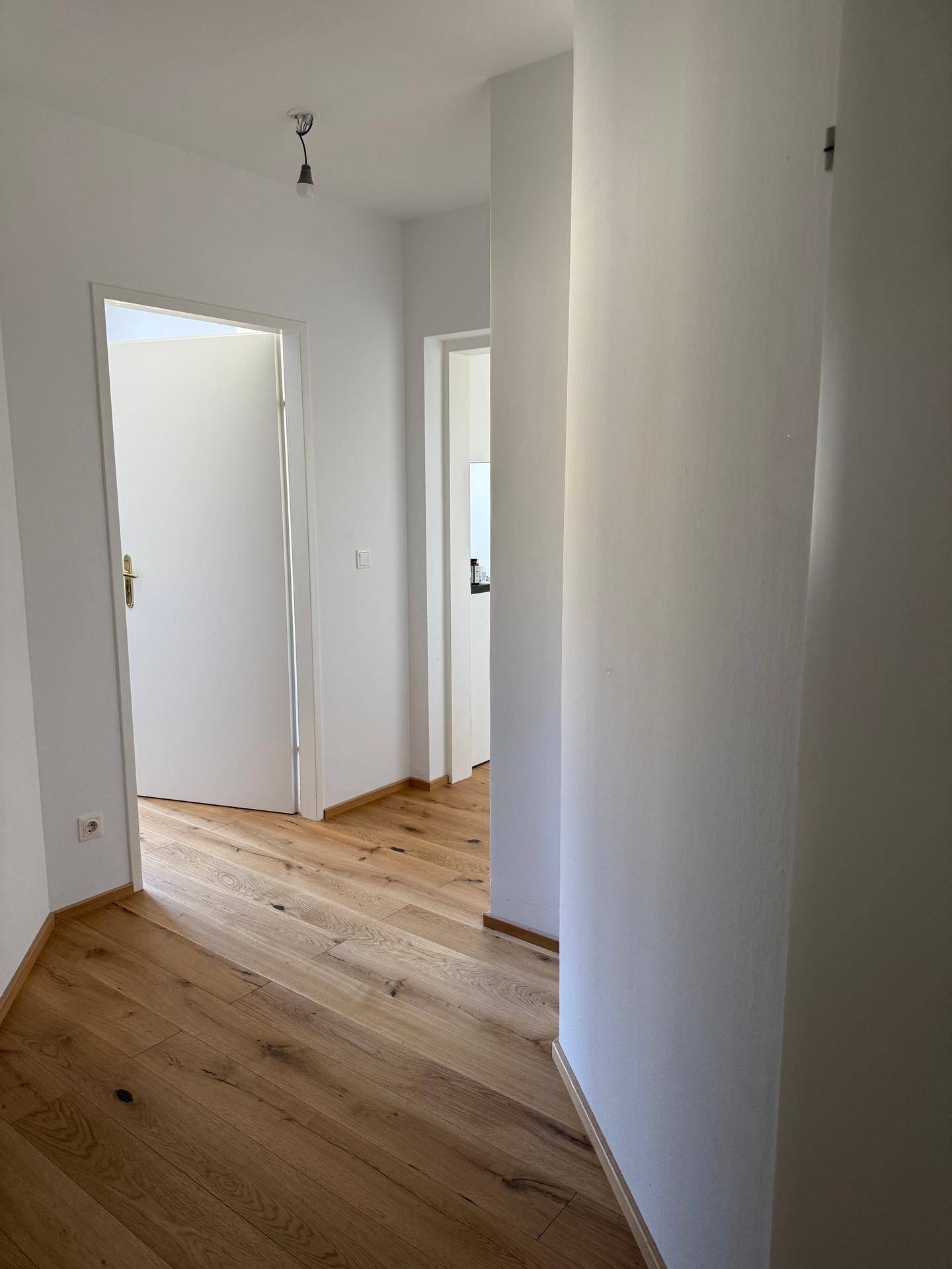 Heller Flur mit Holzboden und weißen Wänden, der zu weiteren Räumen führt.