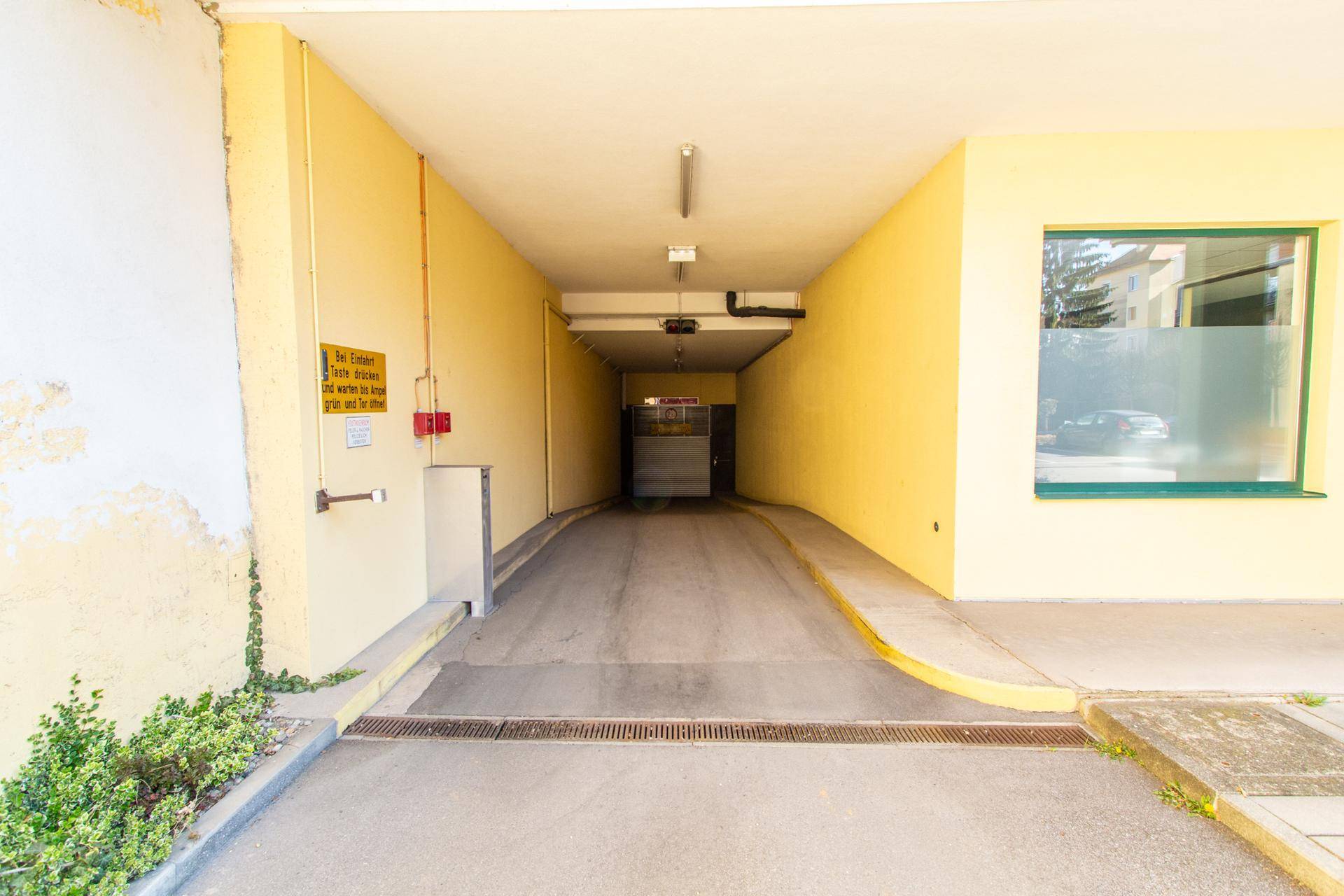 Einfahrt zu einer Tiefgarage mit Rampe und gelben Wänden.