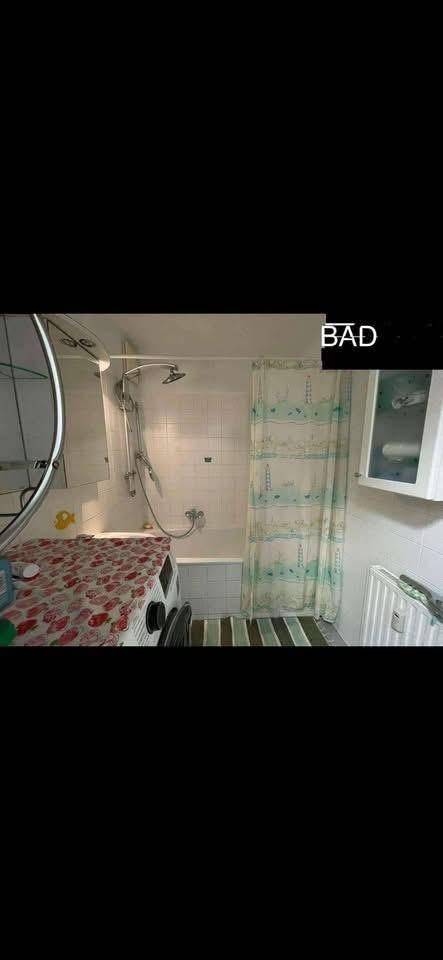 Badezimmer mit Badewanne, Duschvorhang und Waschmaschine, funktional eingerichtet.