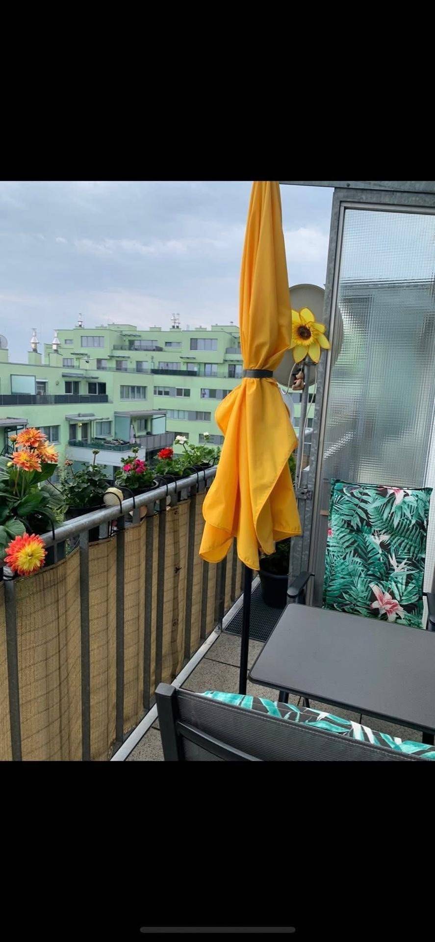 Gemütlicher Balkon mit Sitzgelegenheiten, gelbem Sonnenschirm und Blumenkästen.