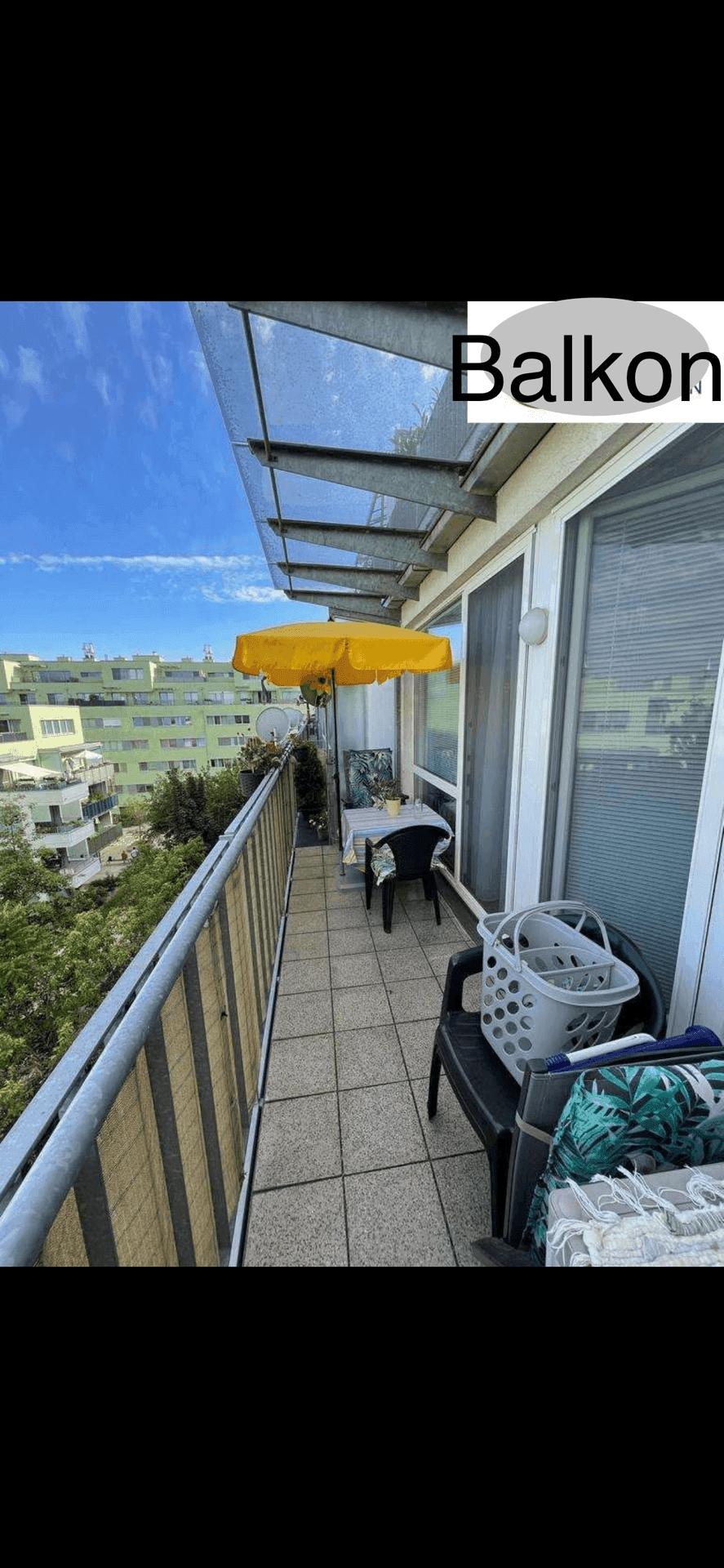 Geräumiger Balkon mit Fliesenboden, Sitzgelegenheiten und gelbem Sonnenschirm, mit Stadtblick.