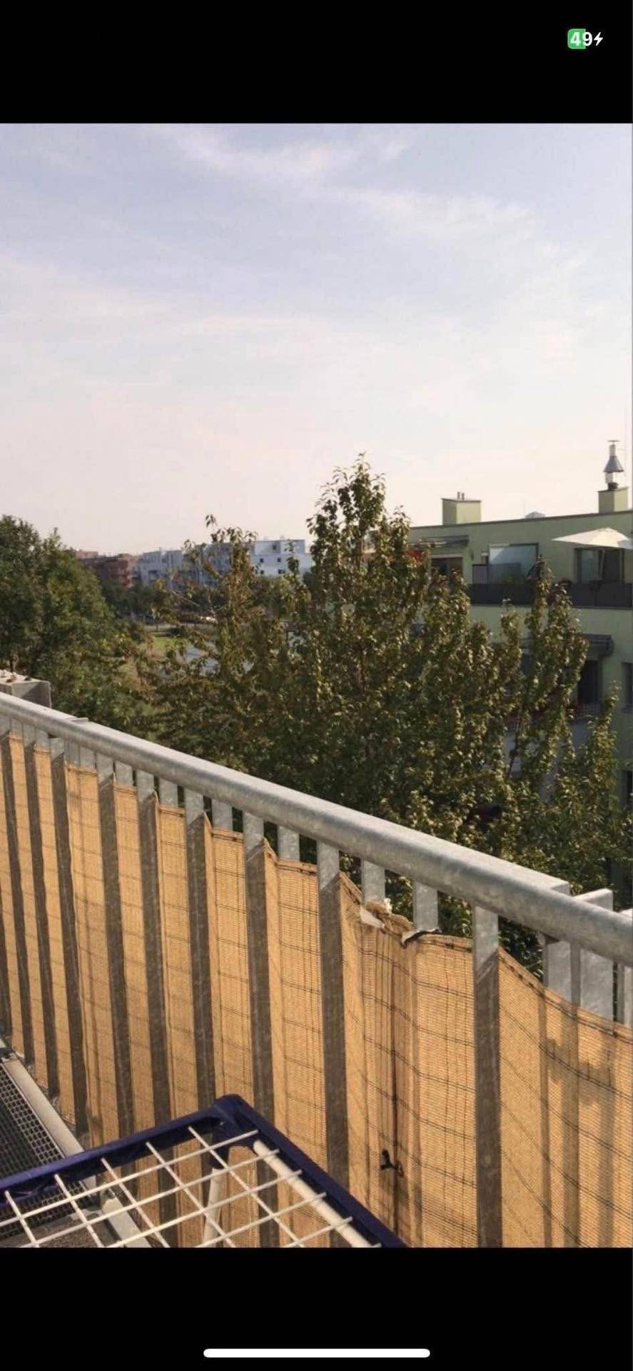 Balkon mit Blick auf grüne Bäume und umliegende Gebäude unter klarem Himmel.