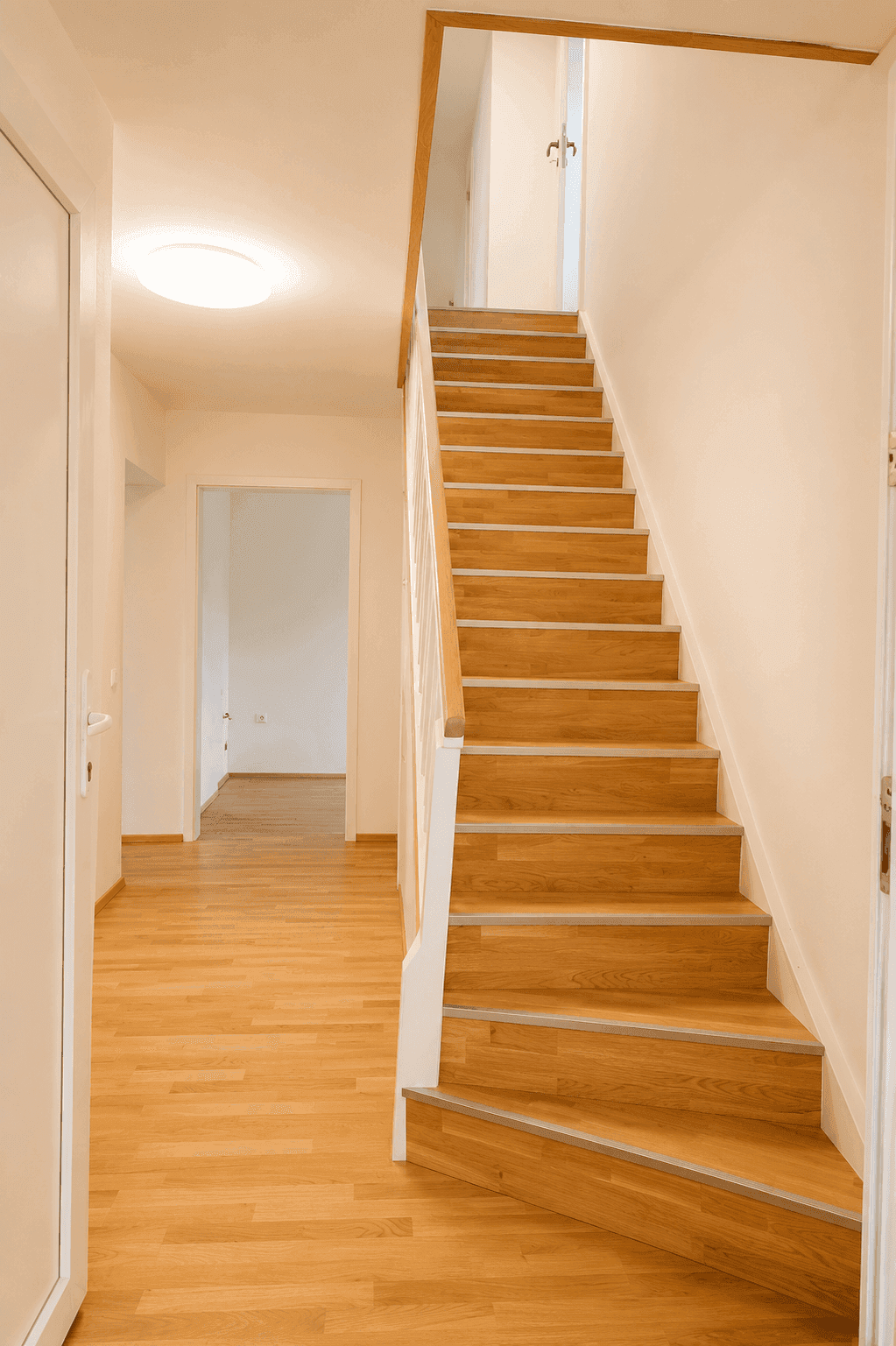 Heller Flur mit Holztreppe und Zugang zu weiteren Räumen im Erdgeschoss.