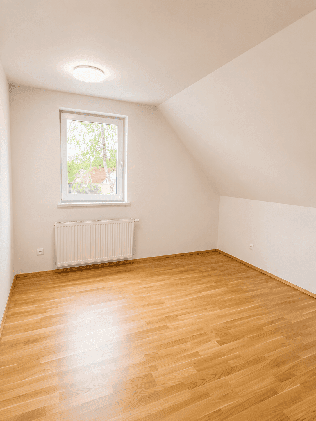 Gemütliches Schlafzimmer im Dachgeschoss mit Parkettboden, Fenster und Dachschrägen.